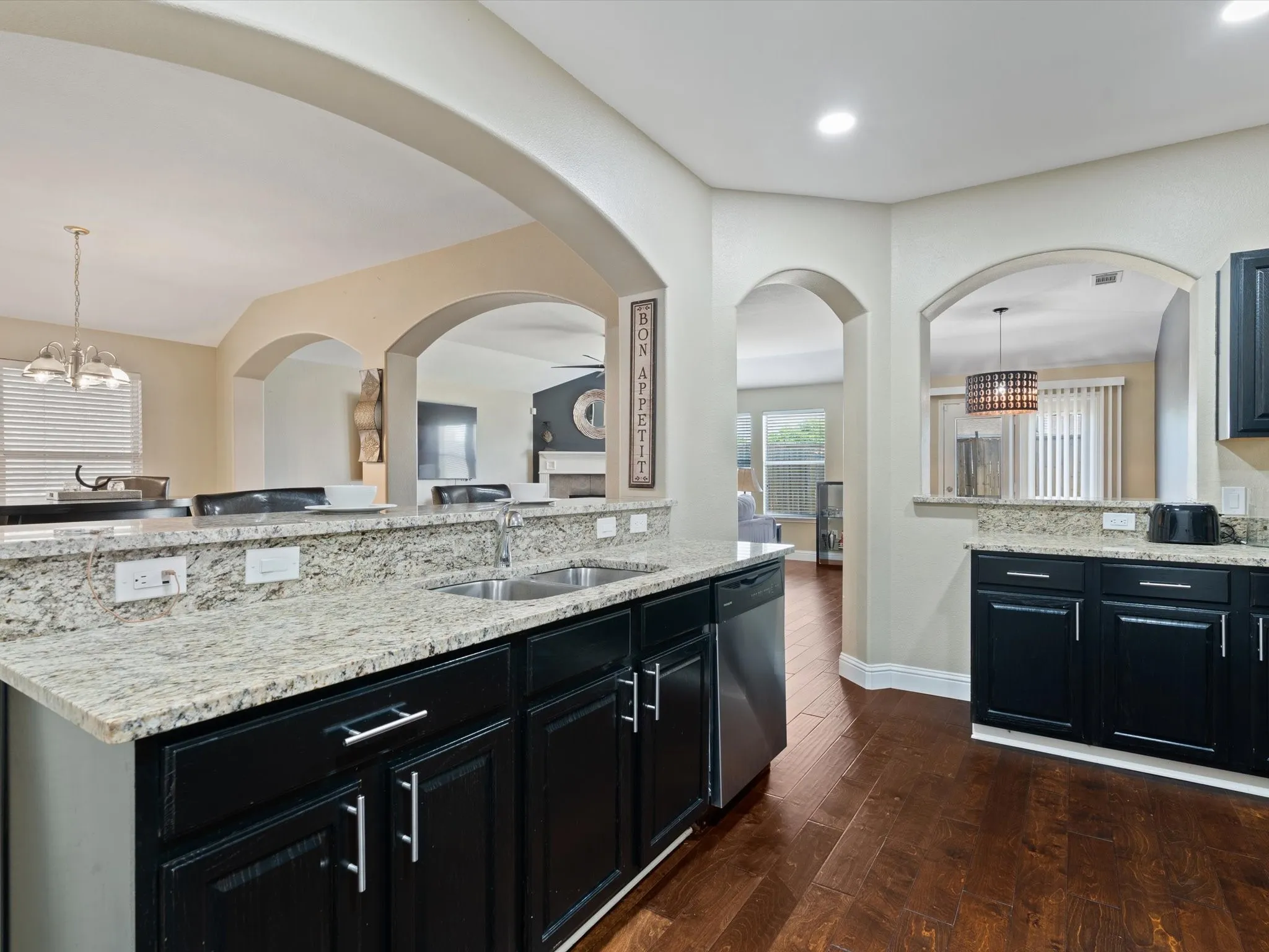 Kitchen featuring sink, dishwasher, light stone countertops, and dark wood-type flooring