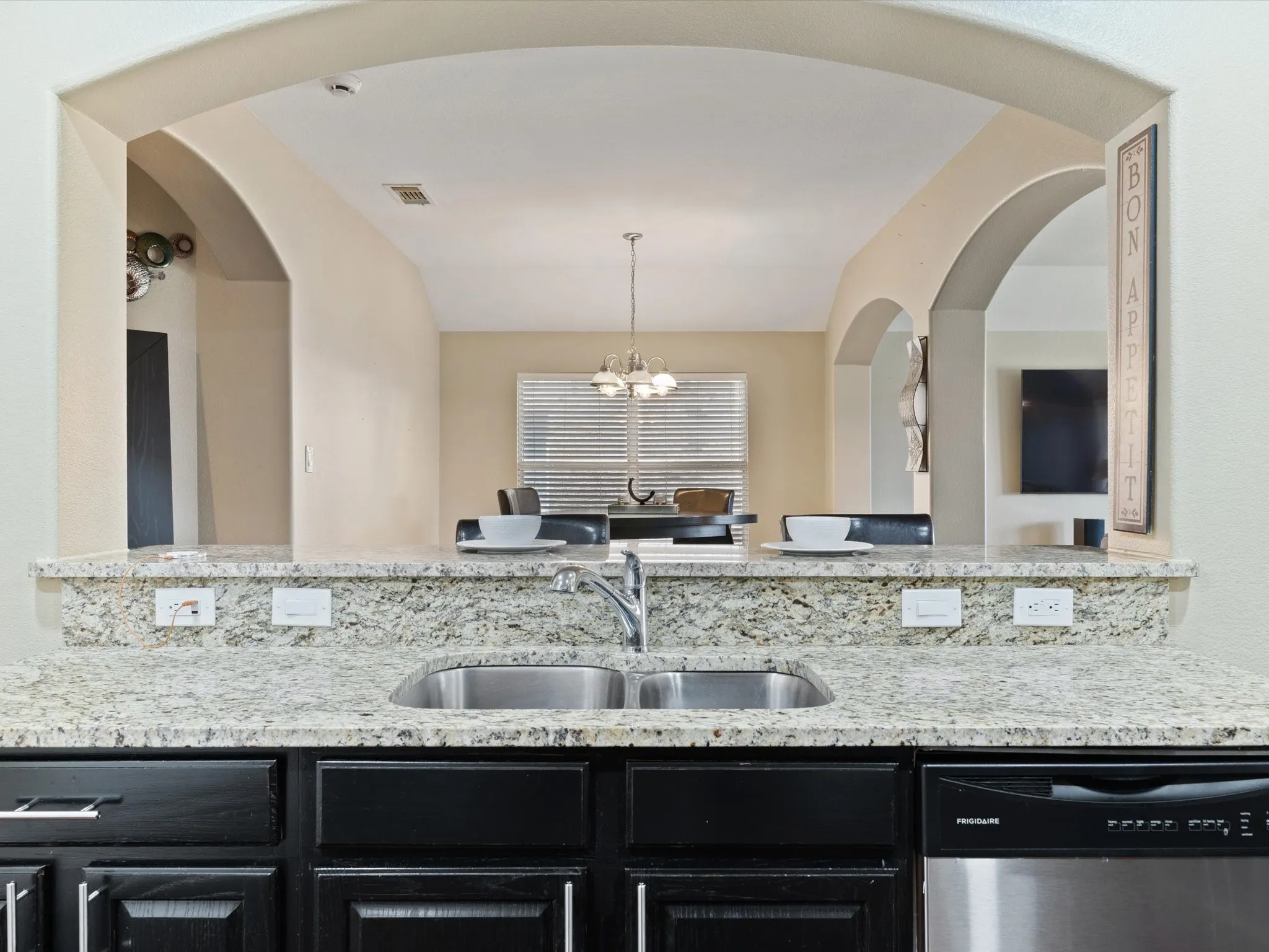 Kitchen with a notable chandelier, light stone counters, stainless steel dishwasher, decorative light fixtures, and sink