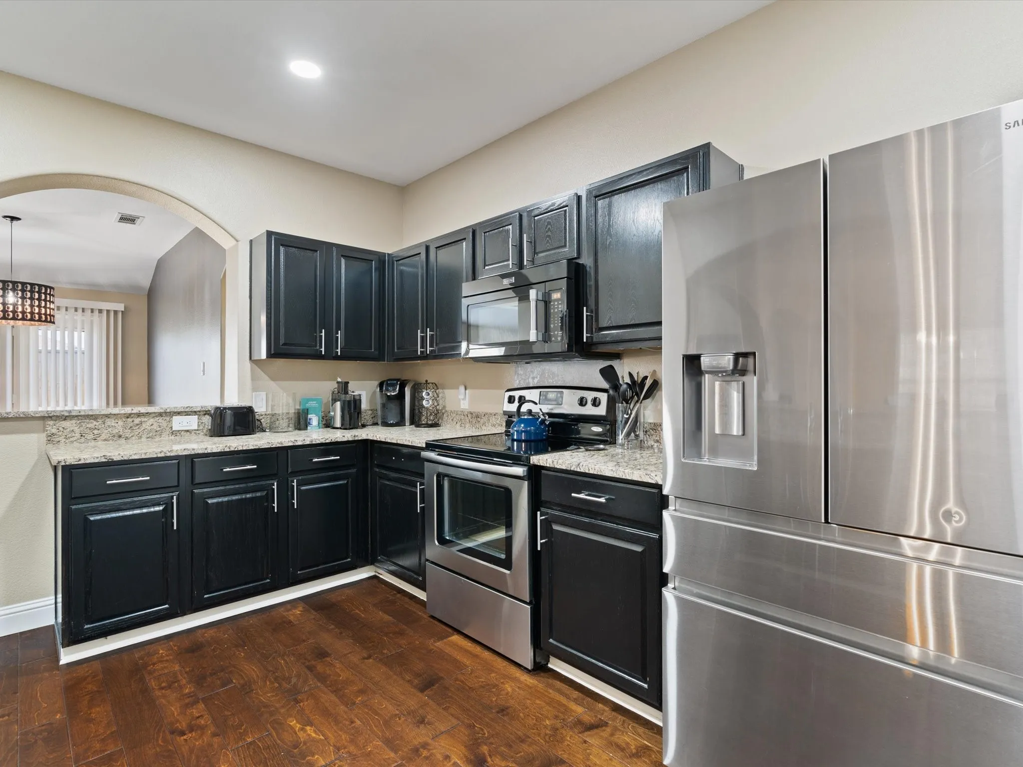 Kitchen with stainless steel appliances, decorative light fixtures, dark hardwood / wood-style flooring, and light stone counters