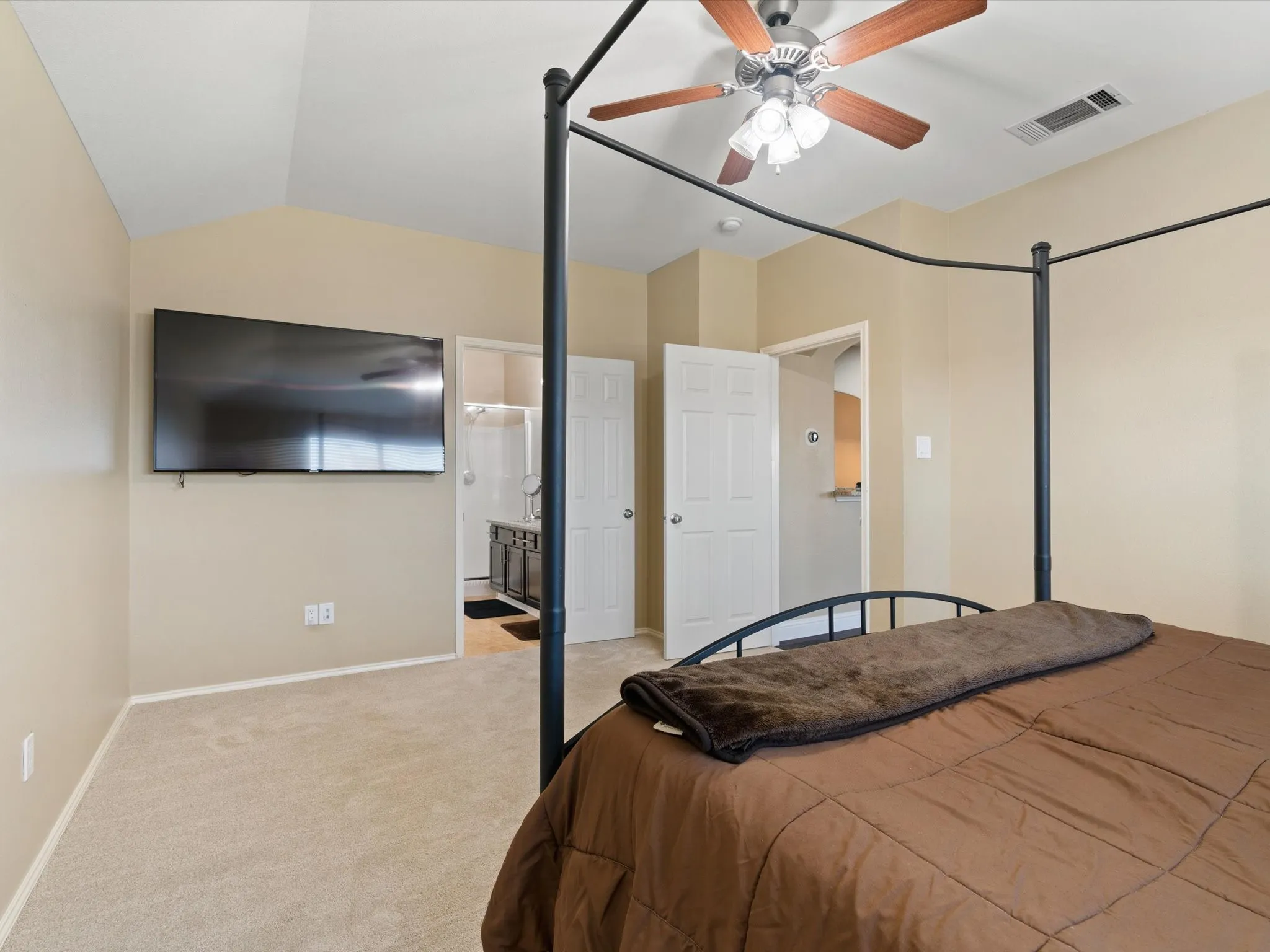 Carpeted bedroom featuring ensuite bath, ceiling fan, and vaulted ceiling