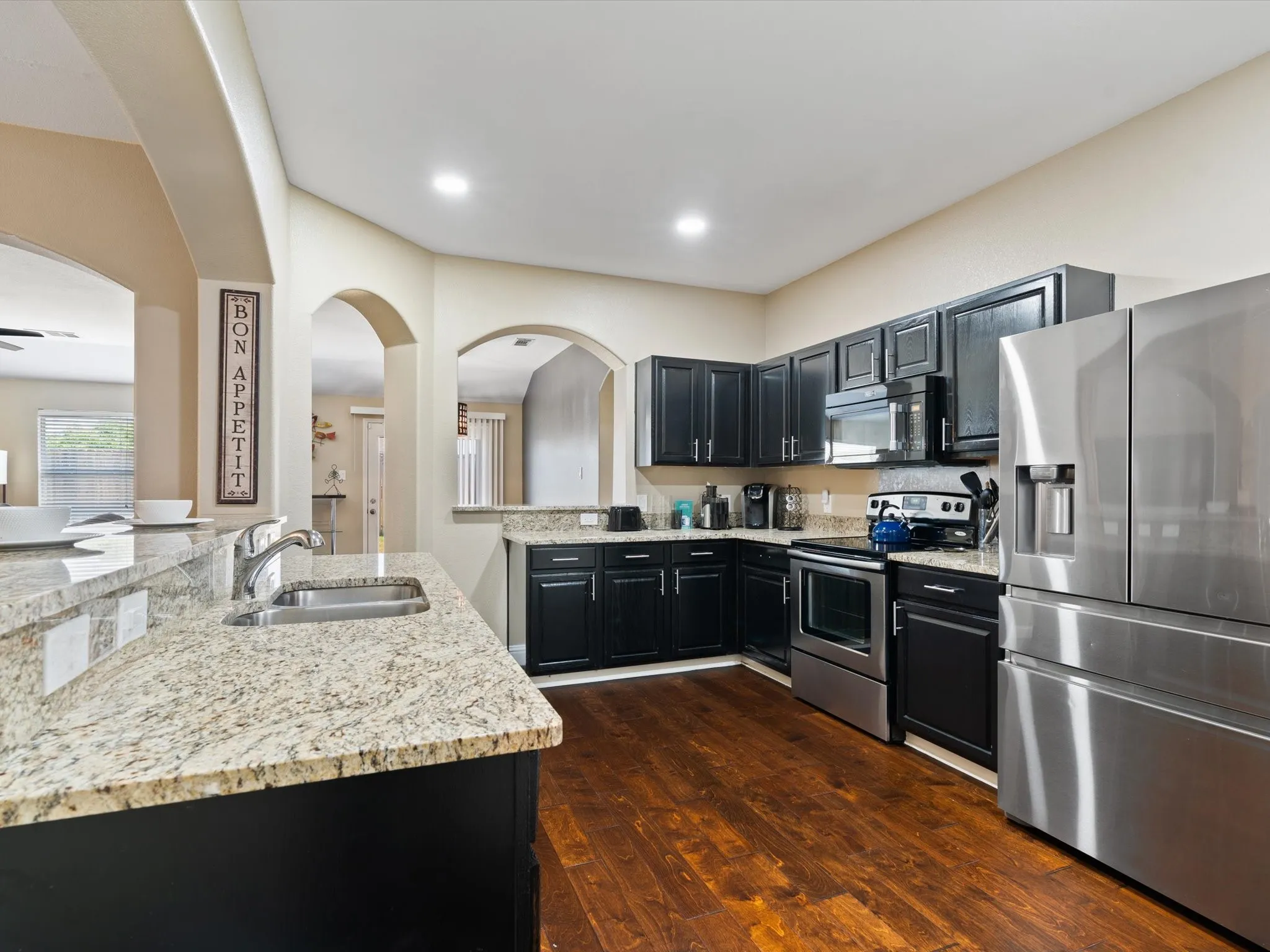 Kitchen with appliances with stainless steel finishes, sink, light stone counters, kitchen peninsula, and dark hardwood / wood-style floors