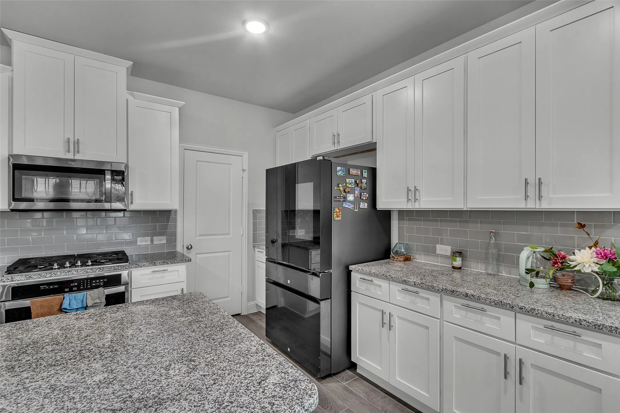 Kitchen with hardwood / wood-style floors, tasteful backsplash, light stone counters, appliances with stainless steel finishes, and white cabinets