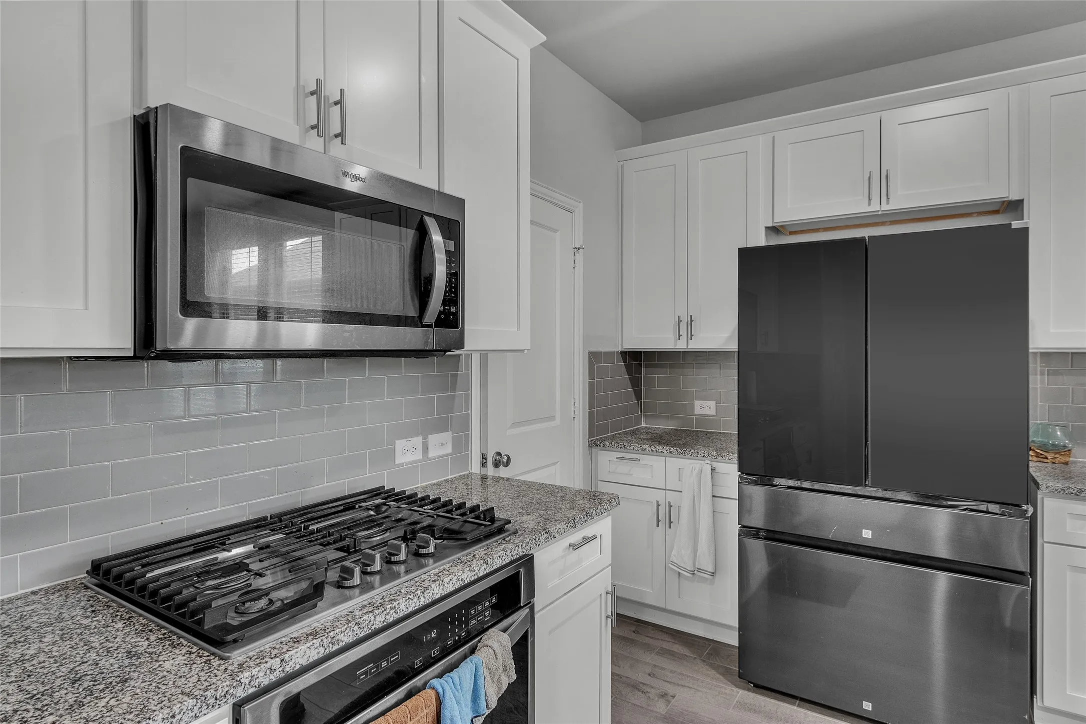 Kitchen featuring backsplash, light hardwood / wood-style floors, stainless steel appliances, light stone counters, and white cabinets