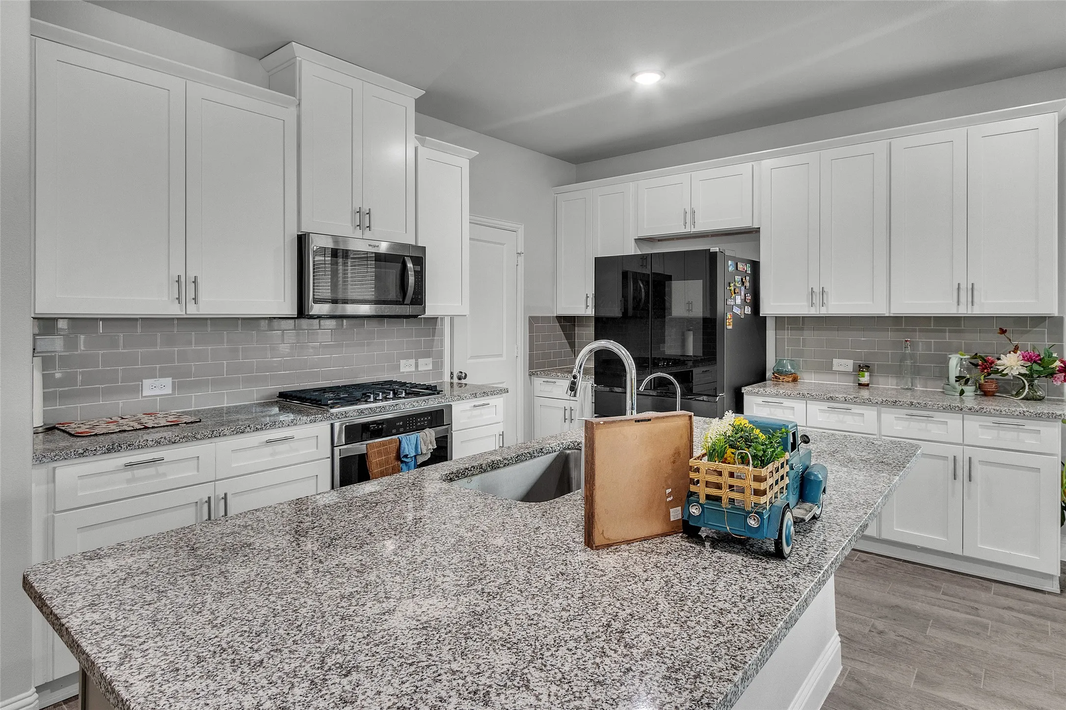 Kitchen with light wood-type flooring, tasteful backsplash, stainless steel appliances, and white cabinetry