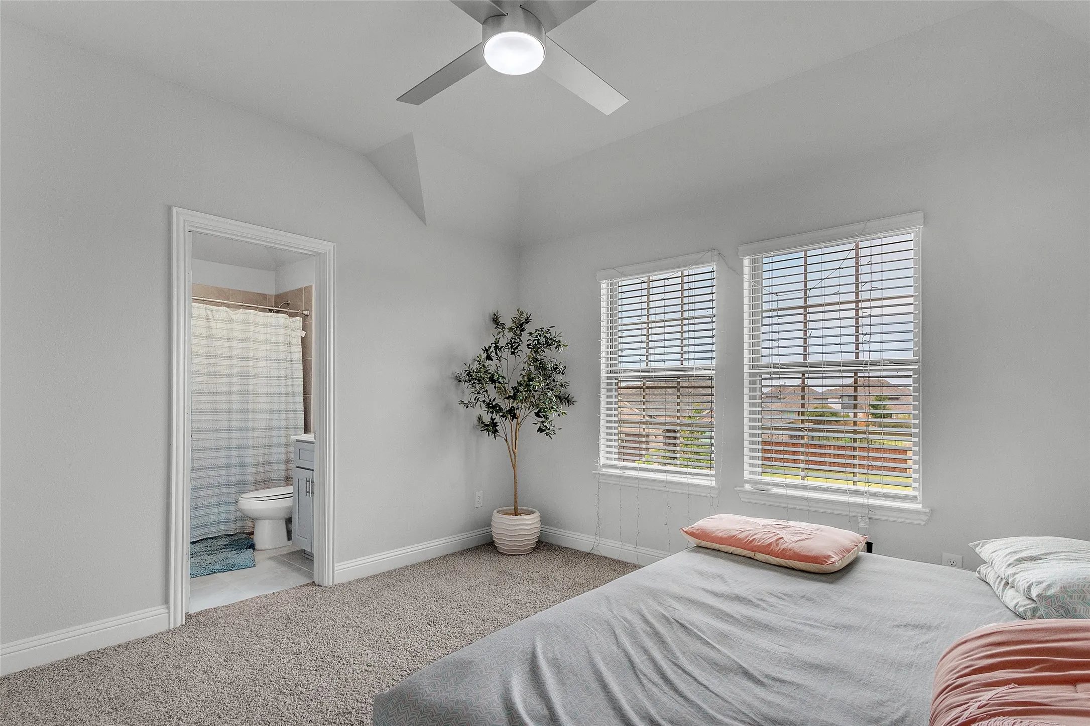 Carpeted bedroom with ensuite bath, vaulted ceiling, and ceiling fan