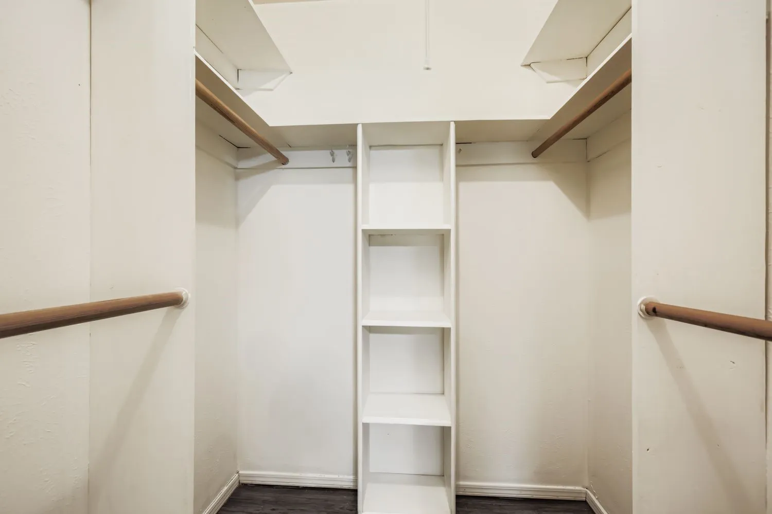 Walk-in closet featuring white built-in shelving, multiple hanging rods, and dark wood-finish flooring