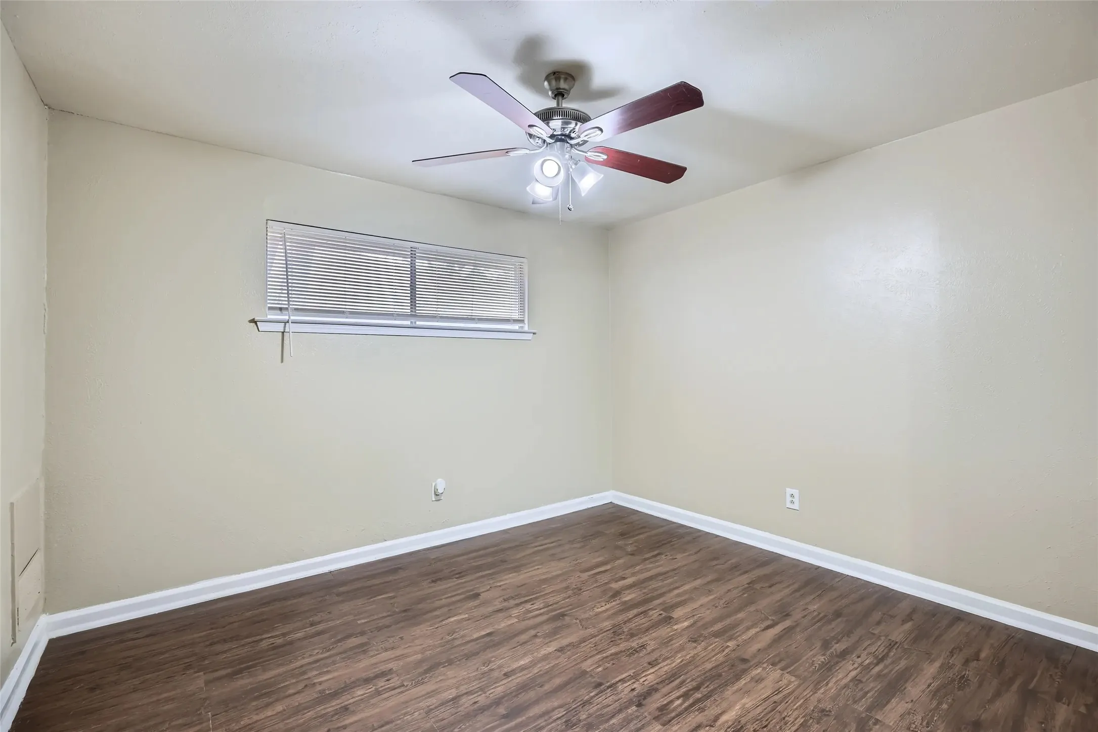 Room featuring wood-finish flooring, a ceiling fan with light fixture, and a window with blinds