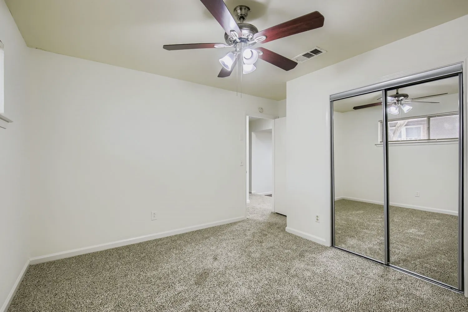 Carpeted room featuring a ceiling fan with integrated lighting, mirrored sliding closet doors, and light-colored walls