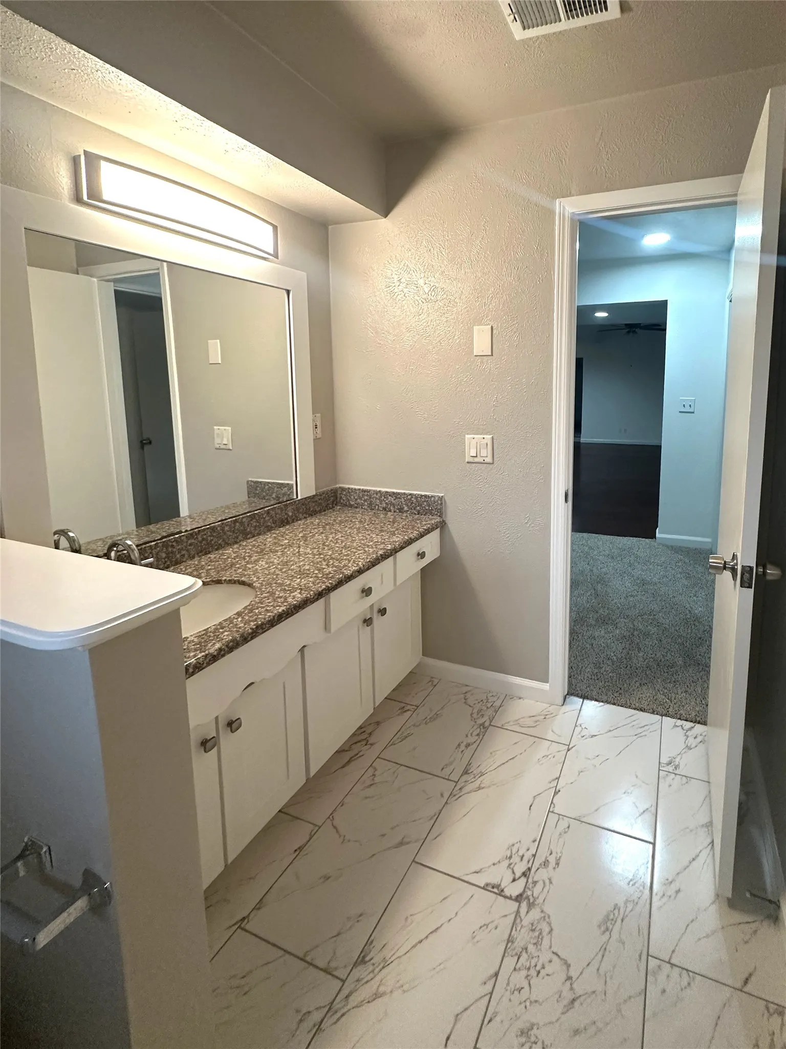 Bathroom vanity featuring a granite-look countertop with an integrated sink, white cabinetry with silver hardware, and a large wall-mounted mirror with overhead lighting