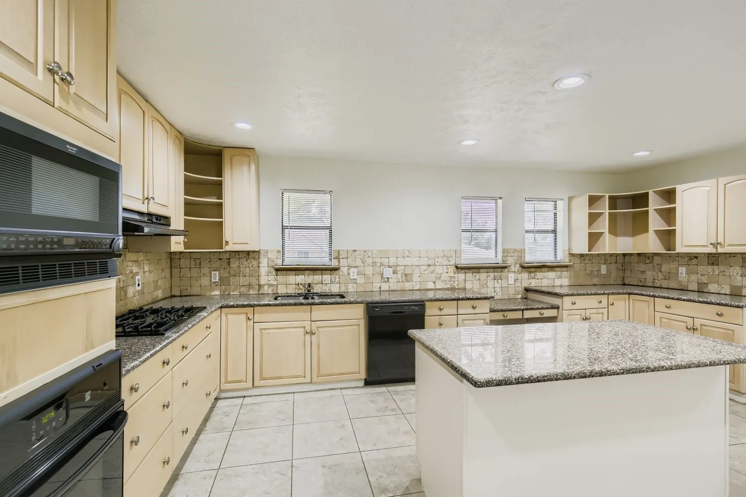 Spacious kitchen featuring an island with a stone countertop, extensive perimeter stone countertops, abundant cabinetry, tile flooring, and integrated black appliances