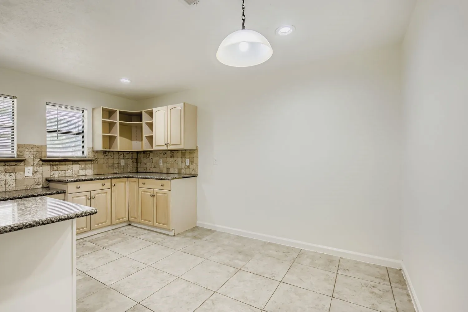 Kitchen area featuring granite-style countertops, light wood-finish cabinetry, and a full tile backsplash