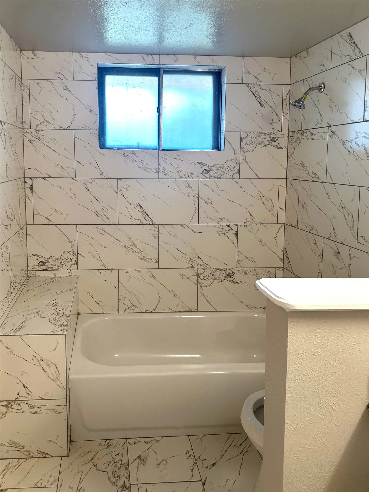 Bathroom featuring a white bathtub, a sliding window, and a wall-mounted shower head