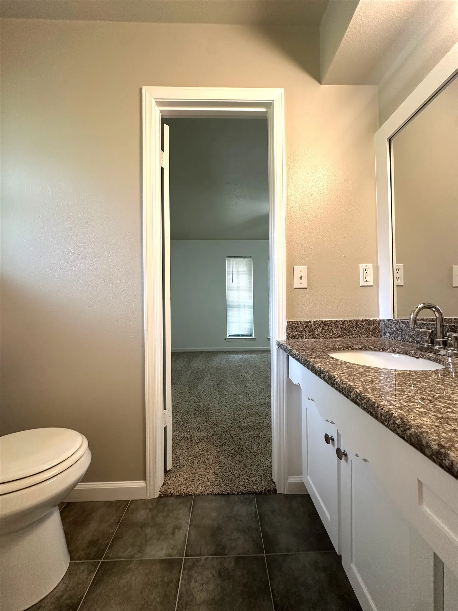 Bathroom vanity featuring a polished stone countertop, undermount sink, and white cabinetry with dark hardware