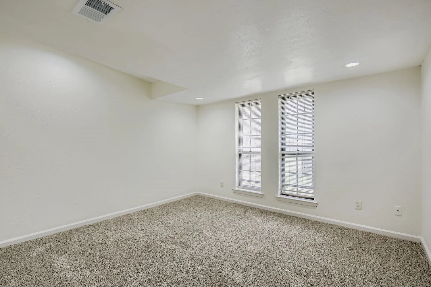 Carpeted room with recessed lighting and two double-hung windows