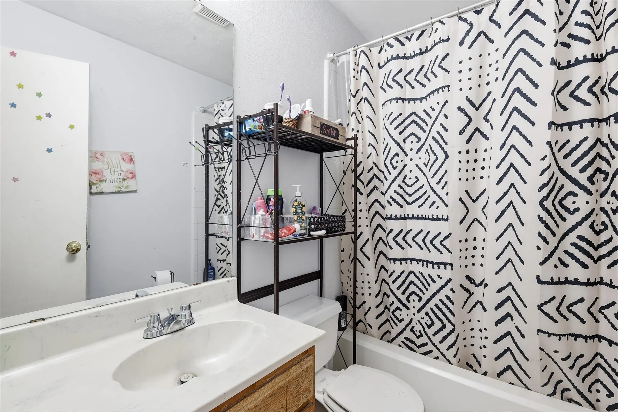 Bathroom featuring a white vanity with integrated sink, chrome faucet, wood-finish vanity base, full-width mirror, and a white bathtub with a white toilet