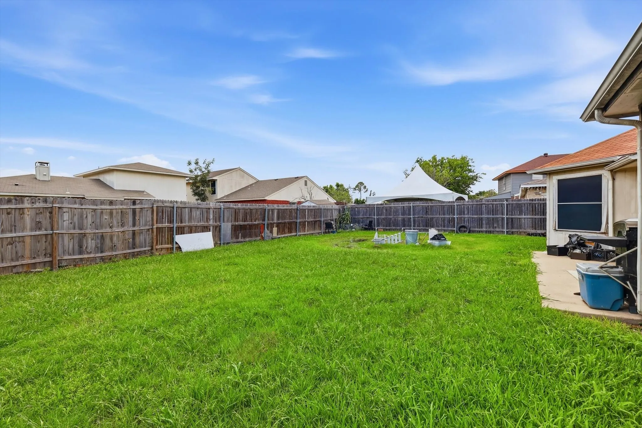 Expansive grassy backyard featuring a full wood privacy fence and concrete patio
