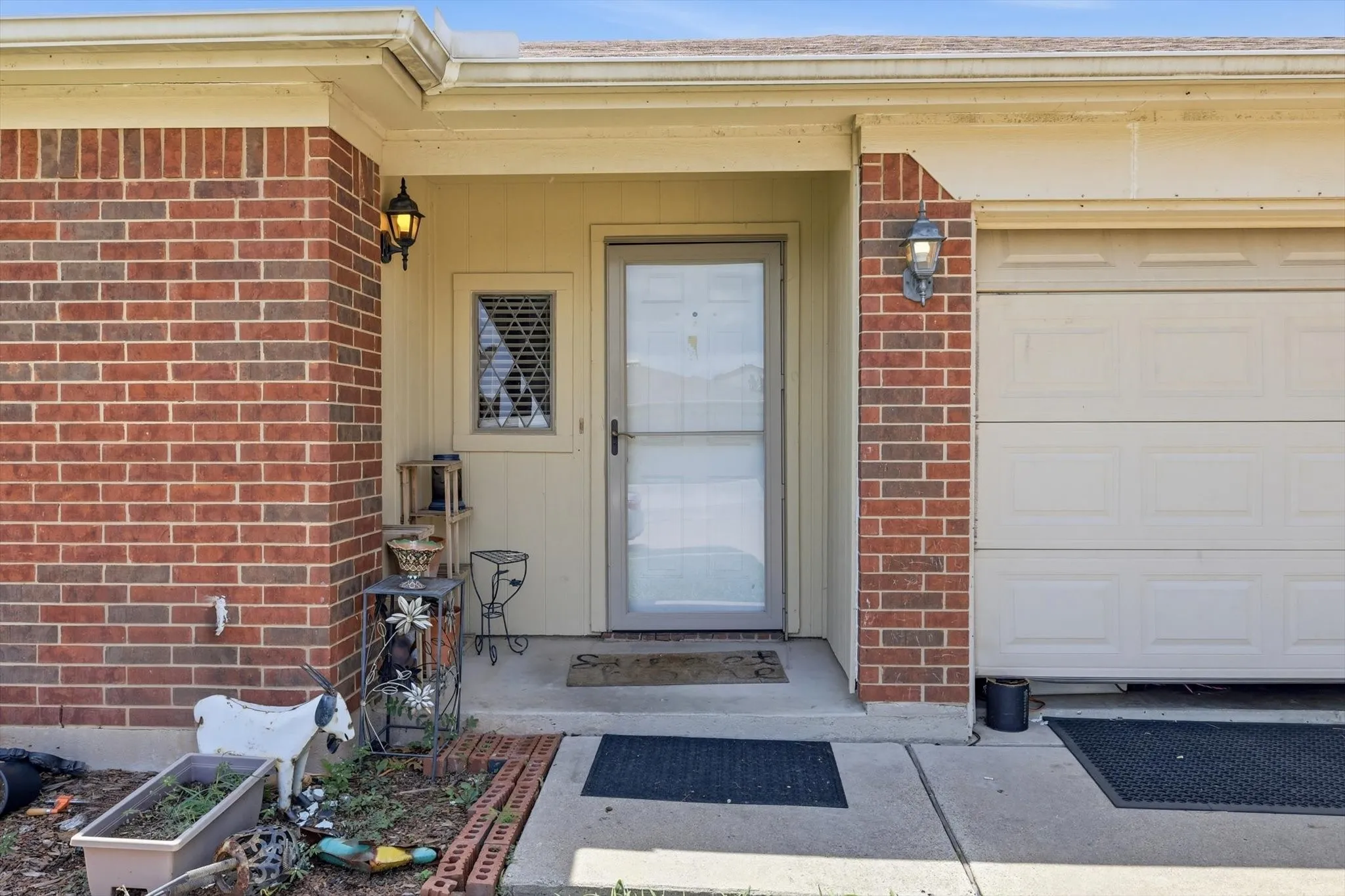 Brick facade entry with a glass storm door, decorative window panel, and exterior lighting fixtures