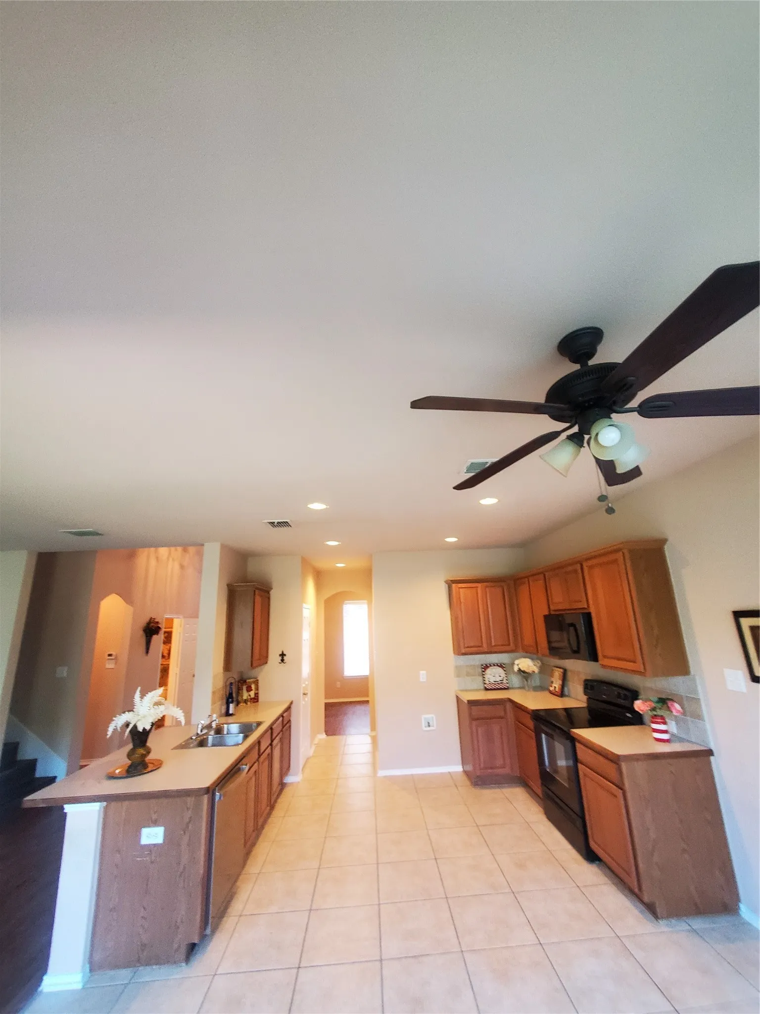 Kitchen featuring stove, kitchen peninsula, dishwashing machine, light tile flooring, and ceiling fan