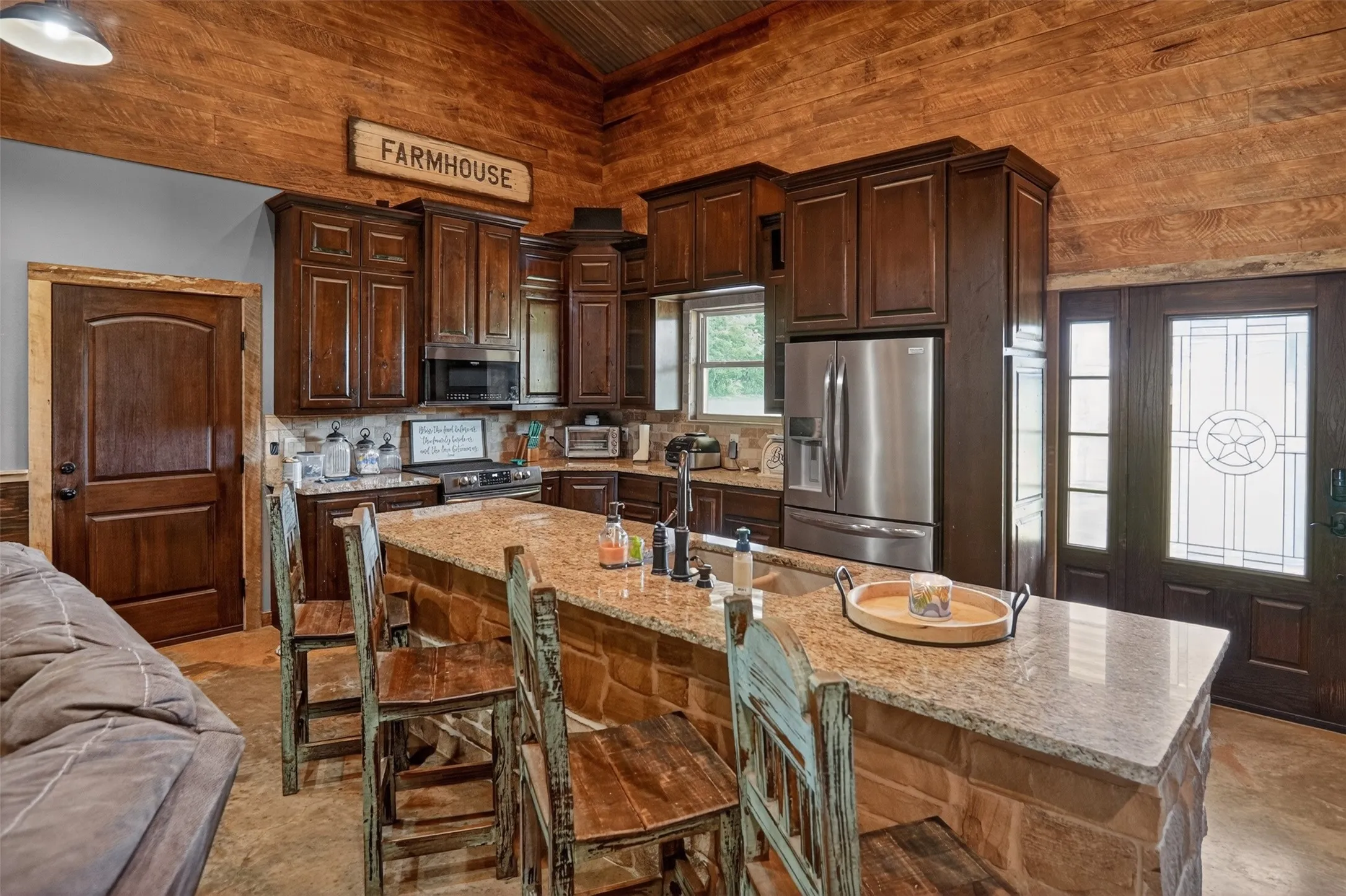 Kitchen featuring a stone-clad island with a granite countertop, dark wood cabinetry, and stainless steel appliances