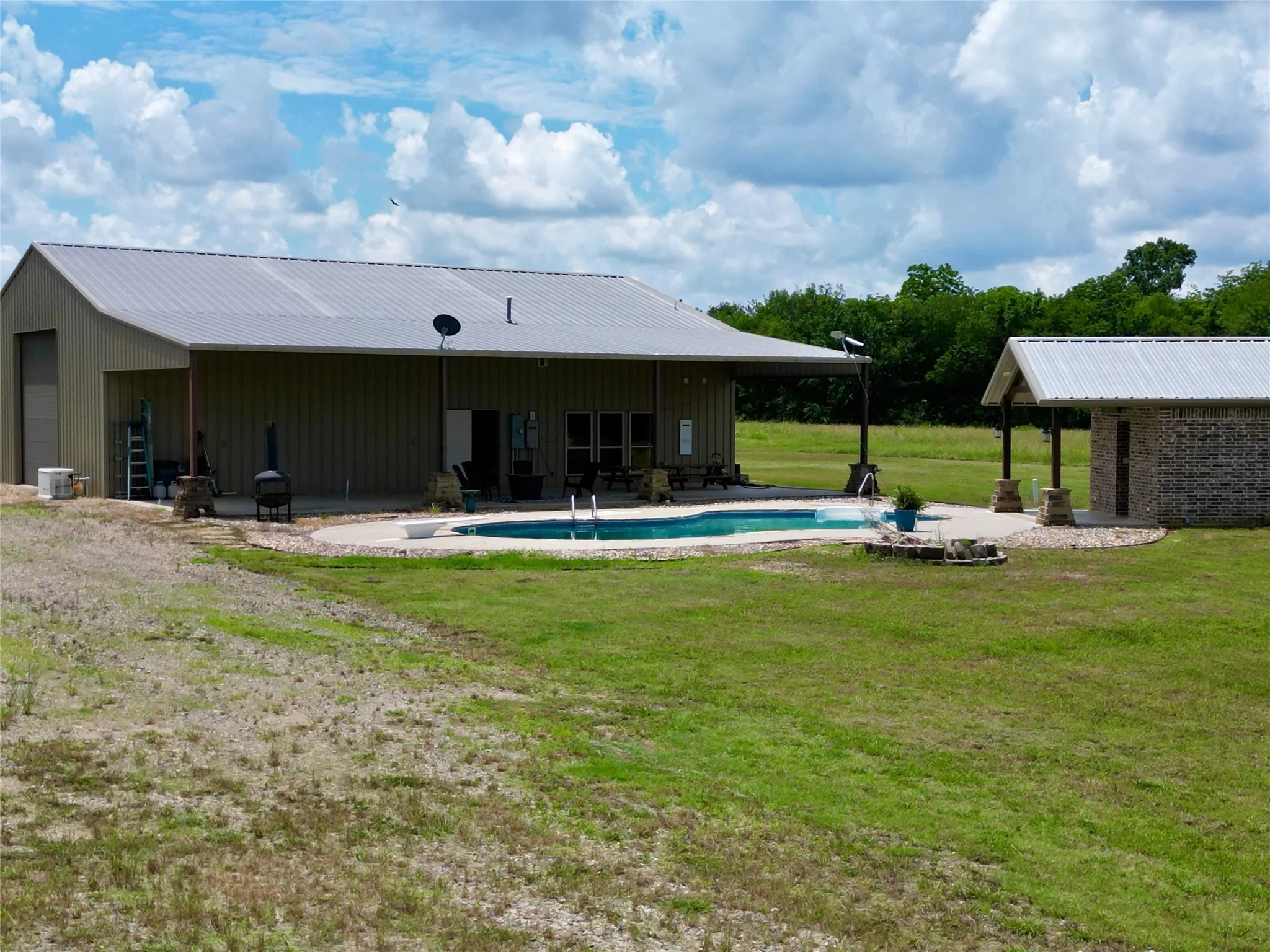 Property featuring an oval-shaped pool with surrounding concrete patio, 20x60 covered back patio with plumbing for outdoor kitchen