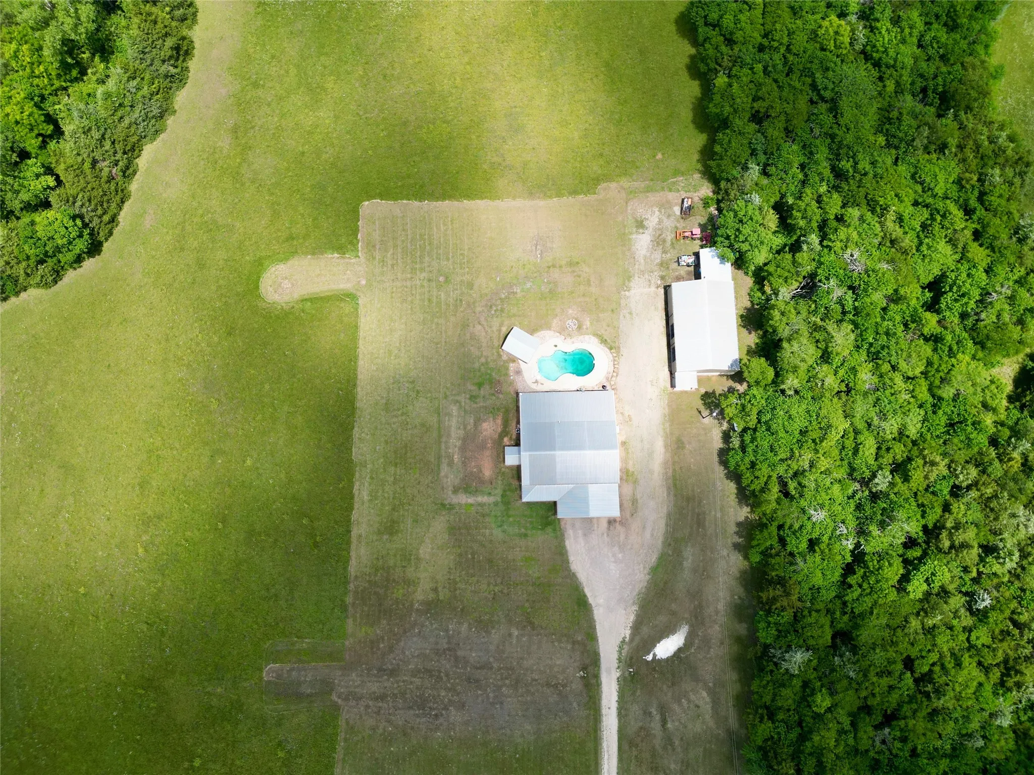 Expansive property with substantial green space, featuring a main residence with a light-colored roof, a freeform swimming pool, and an additional outbuilding
