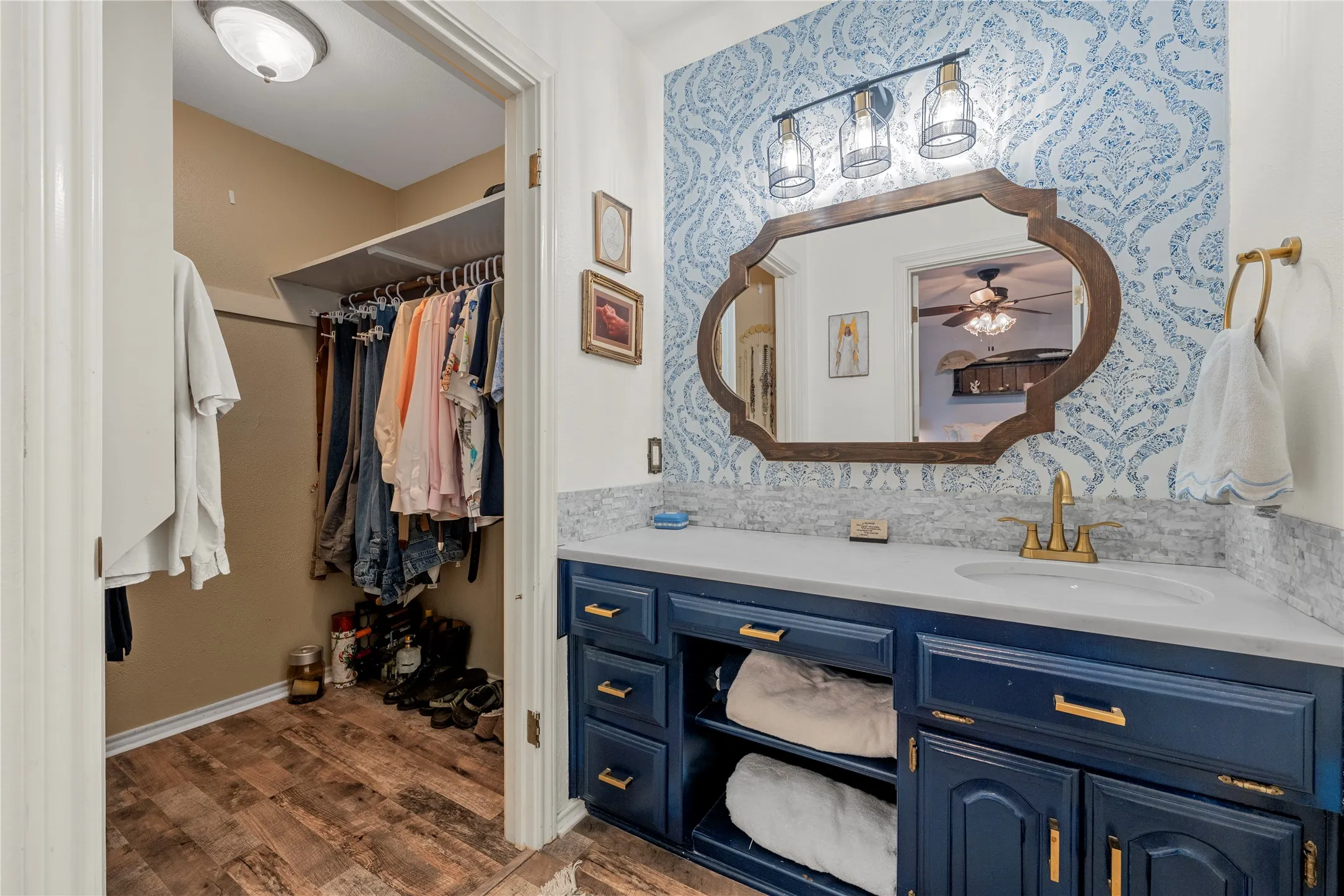Bathroom featuring a blue patterned accent wall, dark blue vanity with brushed brass hardware, white countertop with an undermount sink, and a framed mirror