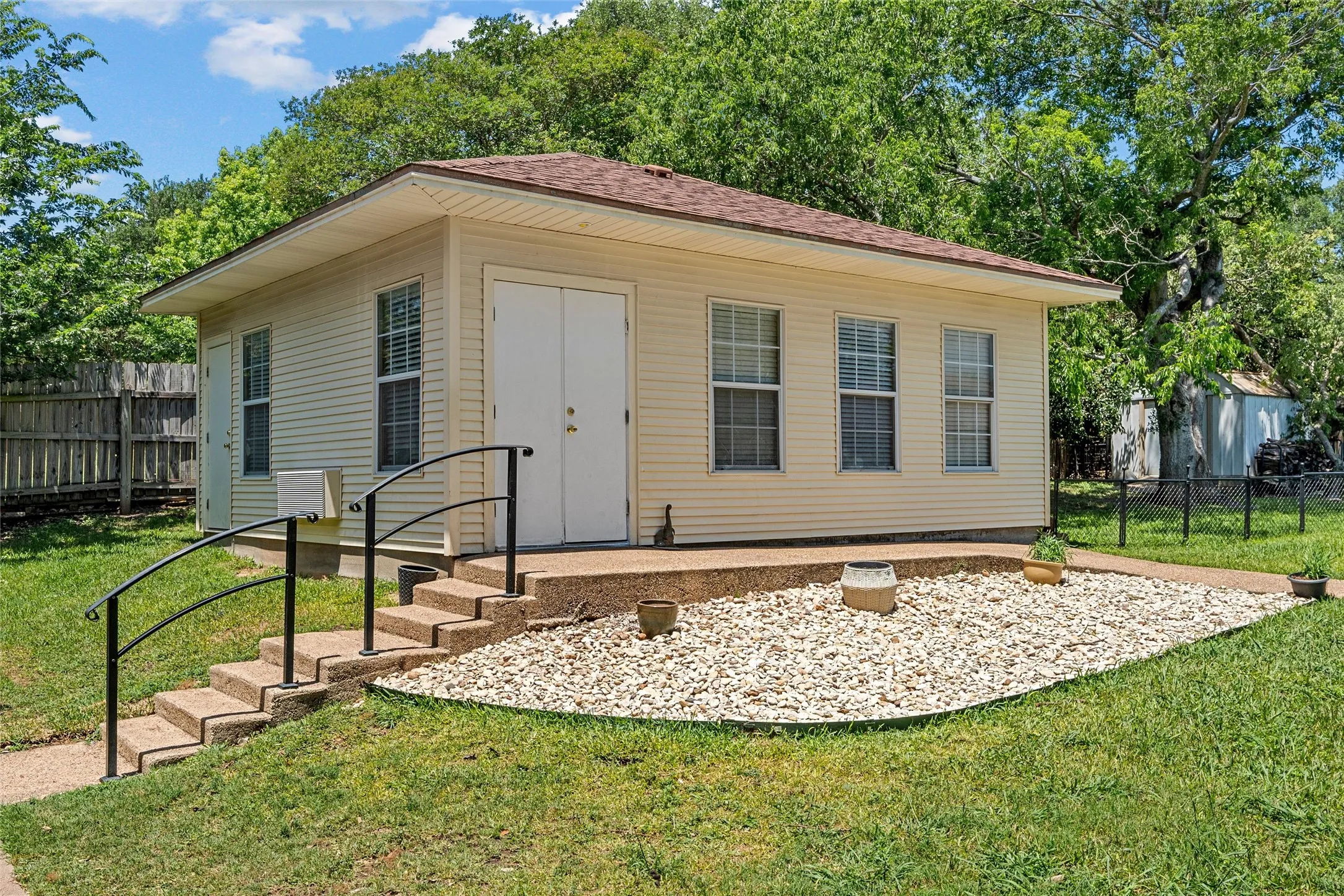 Siding exterior with multiple windows, concrete steps with metal handrails, and a gravel landscaping bed