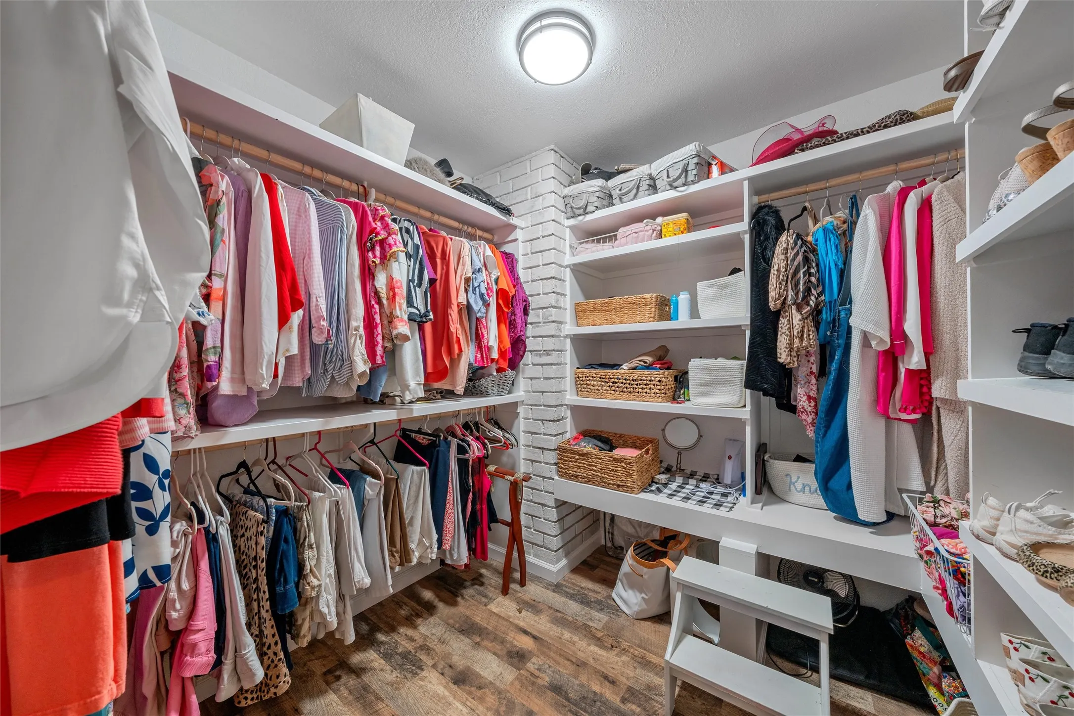 Custom closet system featuring wood-finish flooring, white brick-style wall, and recessed lighting