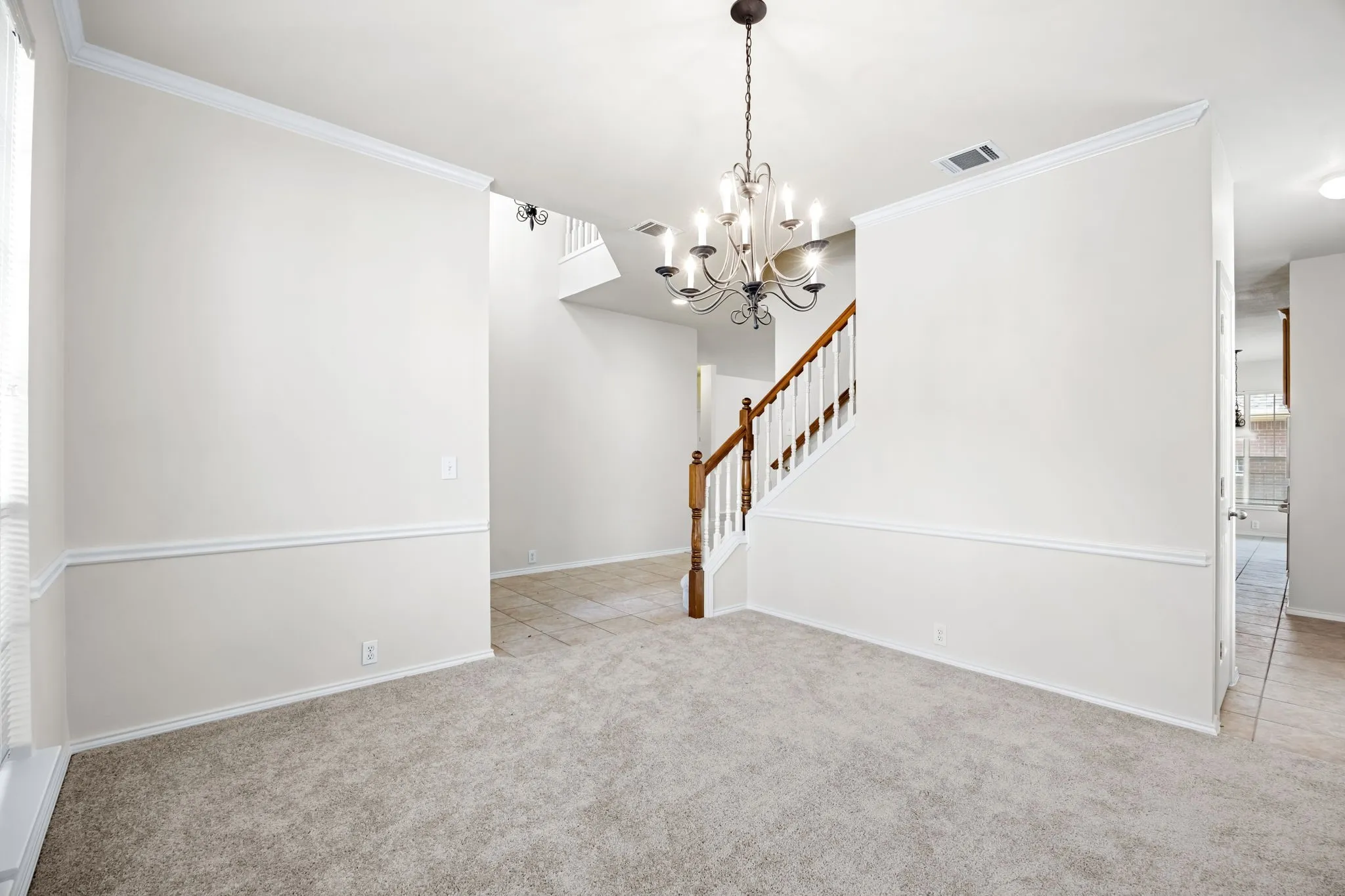 Unfurnished living room with light colored carpet, crown molding, and a chandelier