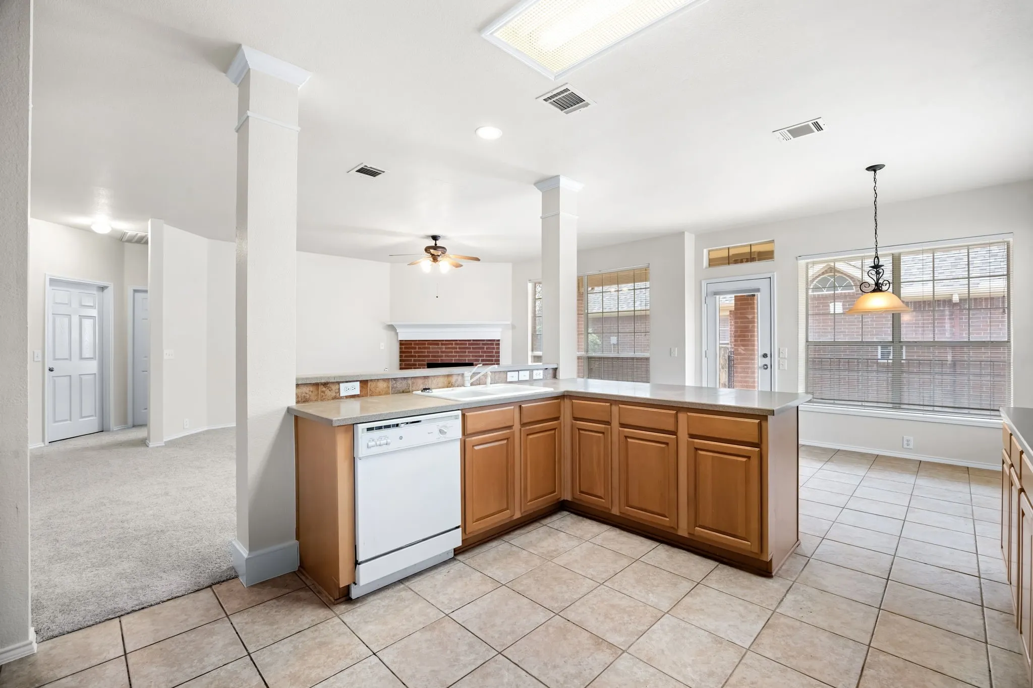 Kitchen featuring white dishwasher, a brick fireplace, light tile patterned floors, light countertops, and open floor plan
