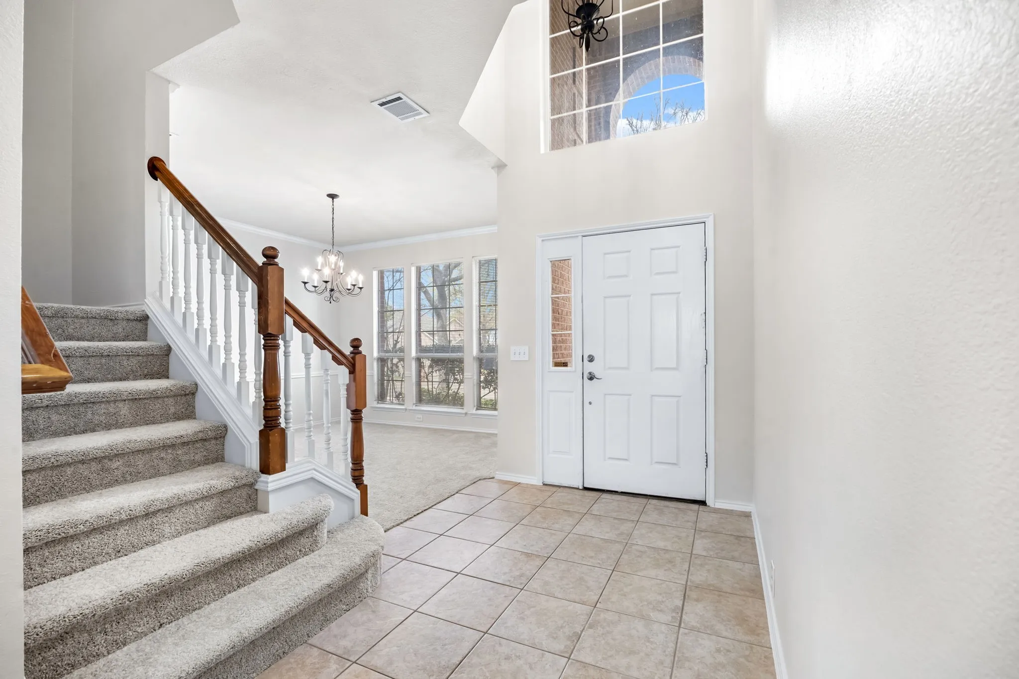 Foyer entrance featuring a chandelier, crown molding, light tile patterned flooring, and light colored carpet