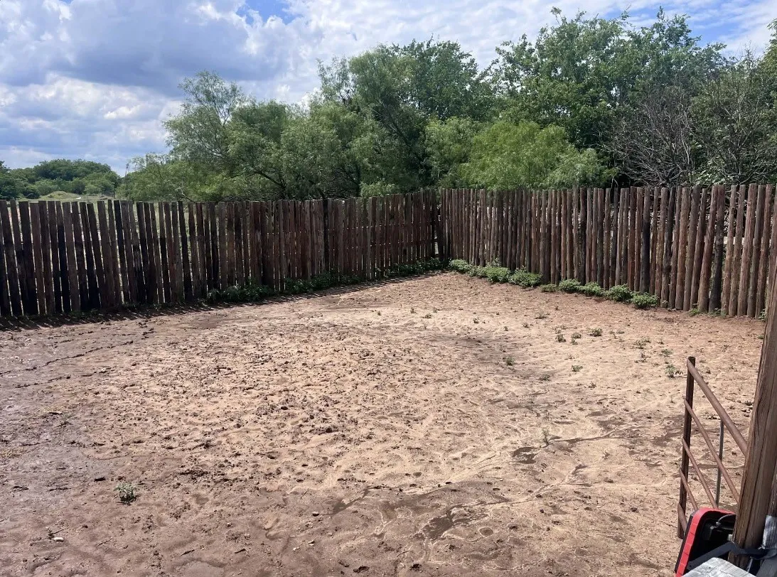 Fenced outdoor area featuring a rustic wood fence, natural ground surface, and mature trees beyond the property line