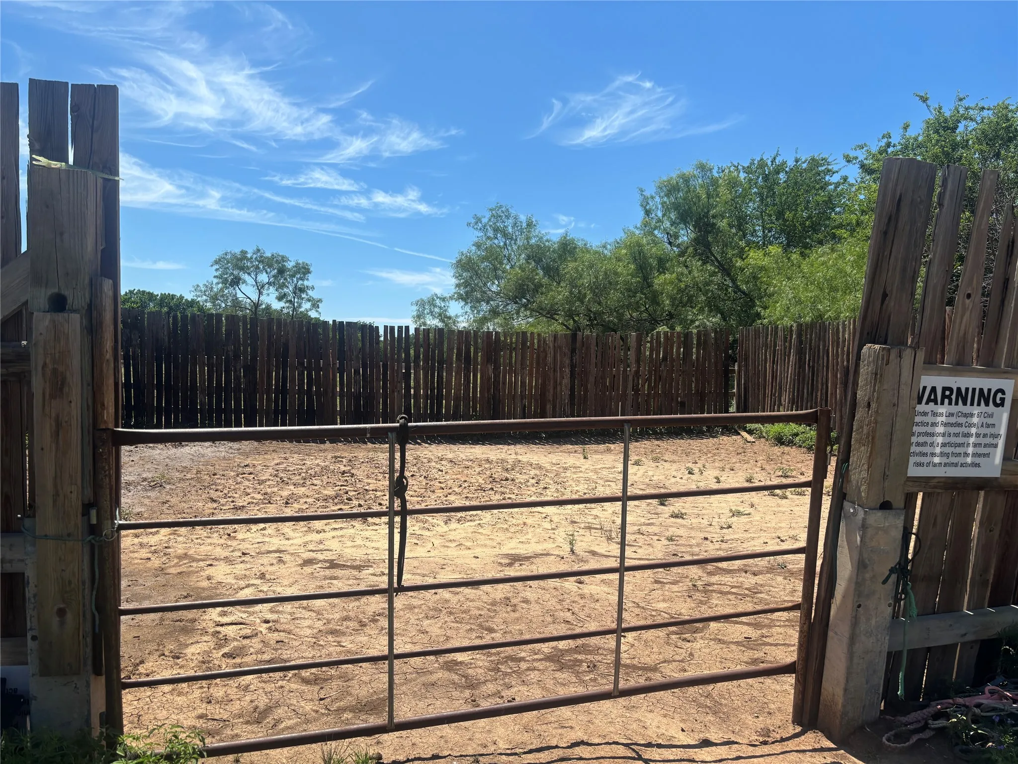 Enclosed outdoor arena featuring a metal gate, sturdy wooden fence posts, and a natural wood perimeter fence