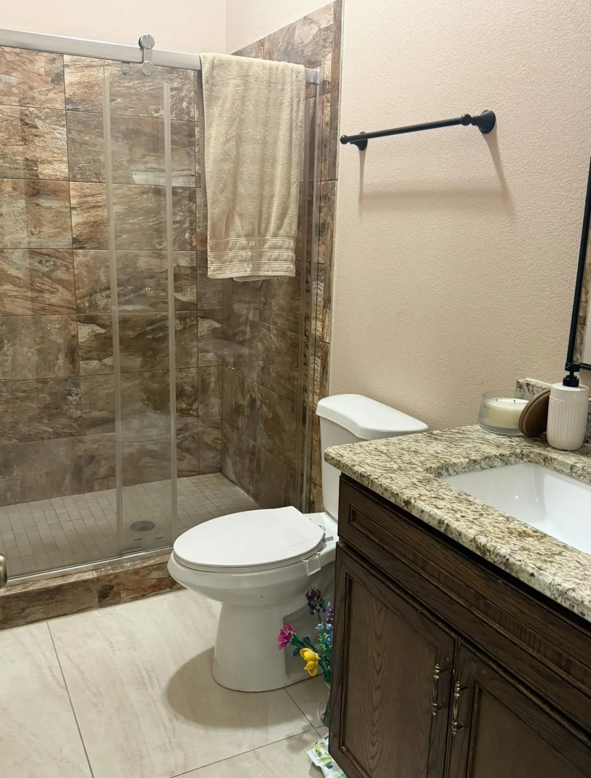 Bathroom featuring a glass-enclosed shower with natural stone-look tile surround, a white toilet, and a vanity with a granite countertop and dark wood cabinetry