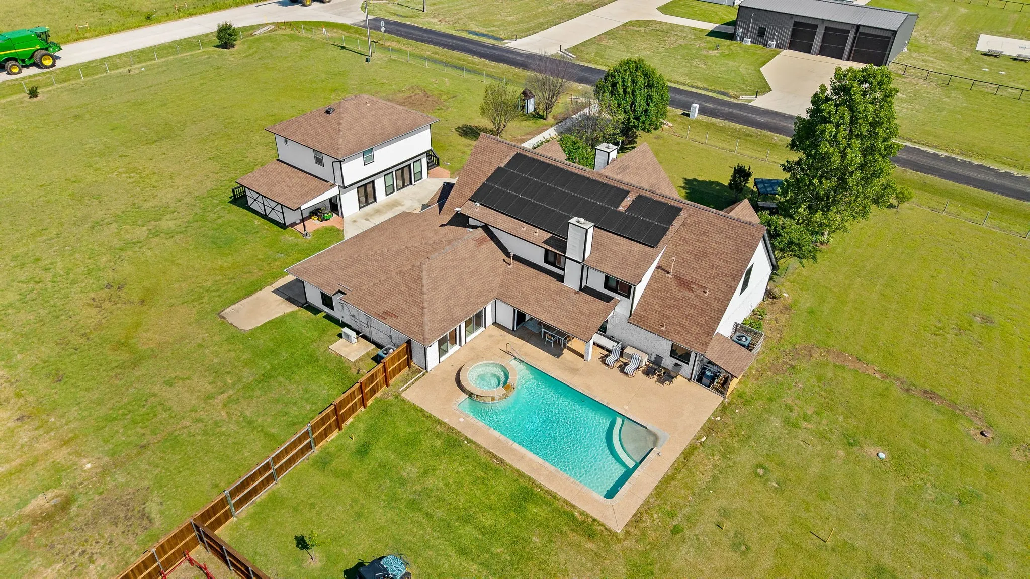 White stucco residence with a brown shingle roof, solar panels, and an in-ground swimming pool with an integrated spa