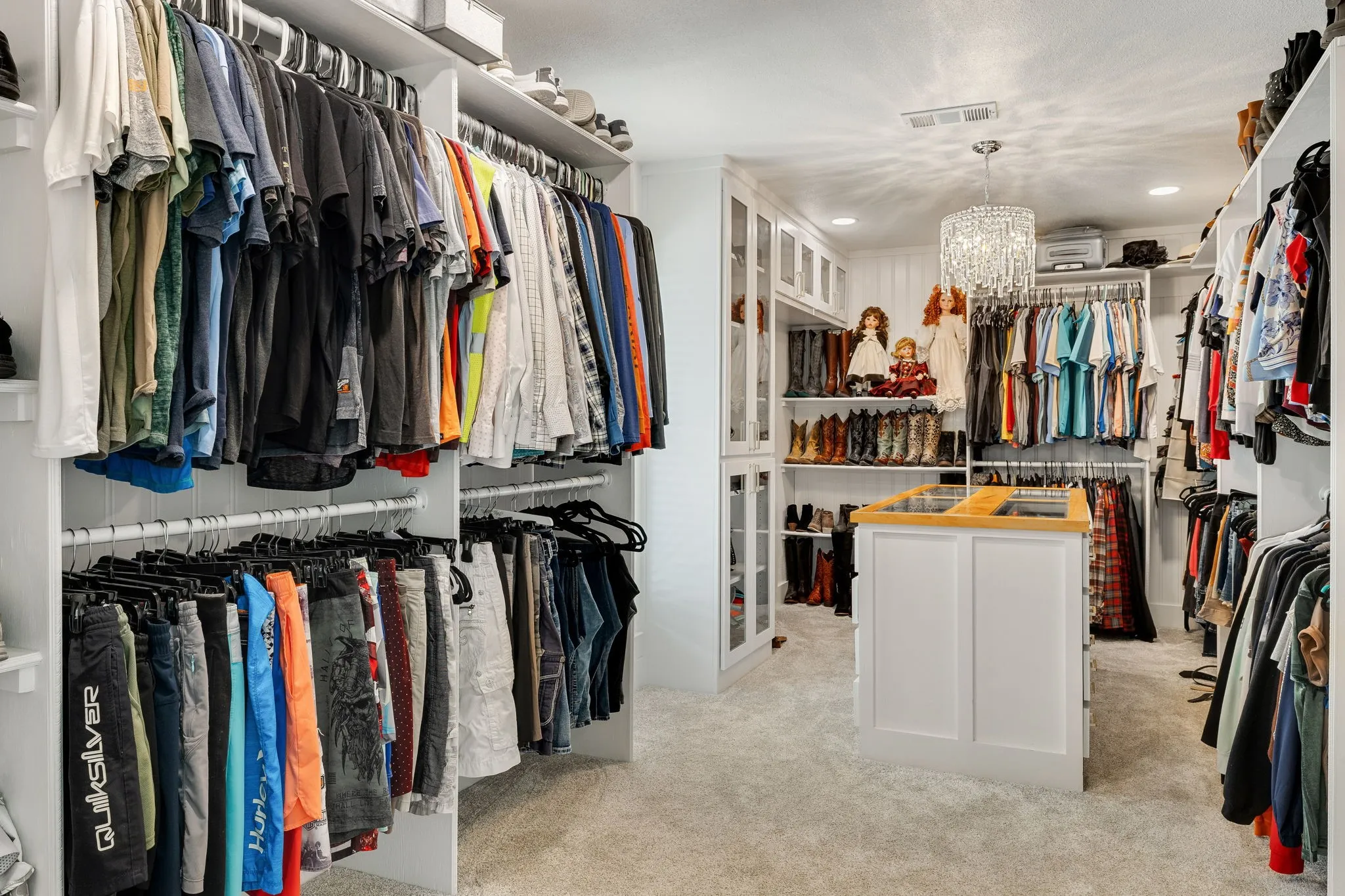 Spacious custom closet featuring extensive built-in shelving, multiple hanging rods, a central island with a wood-finish countertop, recessed lighting, and a decorative chandelier