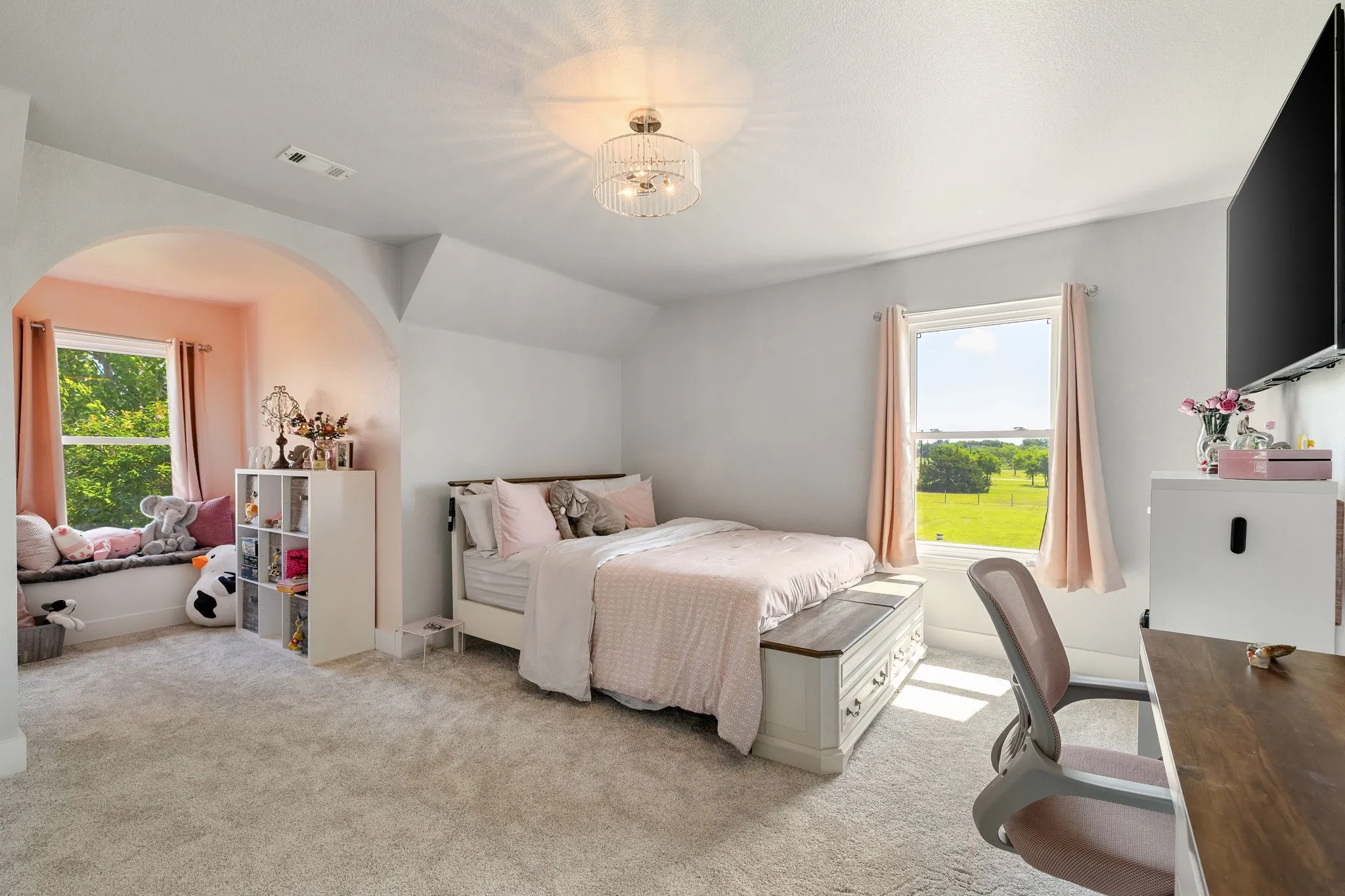 Carpeted bedroom featuring an arched alcove with window seating, a large window offering outdoor scenery, a decorative ceiling light fixture, and light-toned wall finishes