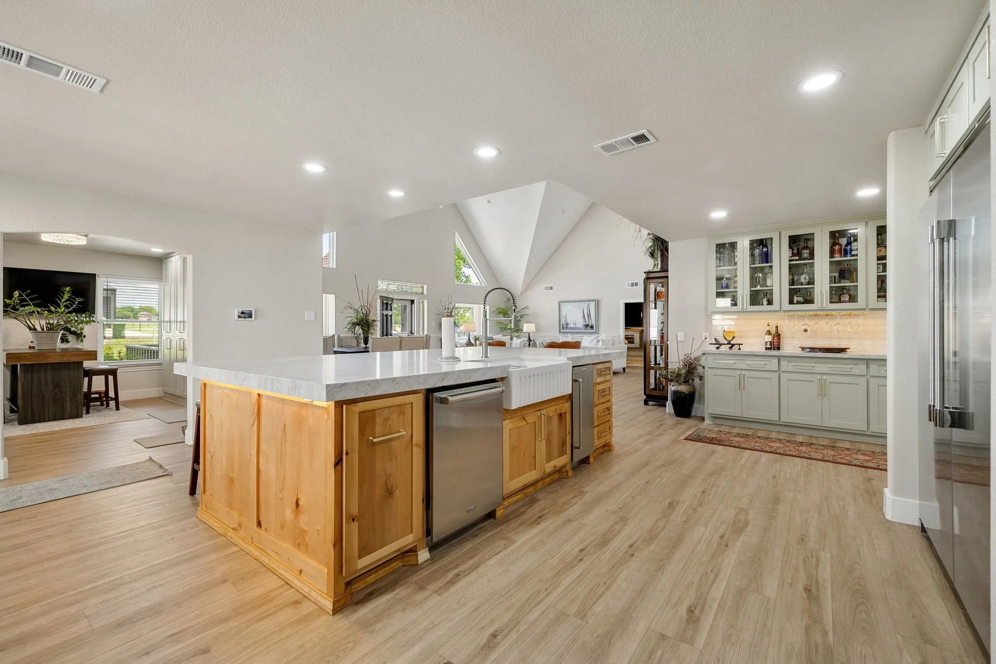 Spacious kitchen featuring a large central island with natural wood cabinetry, a farmhouse sink, and integrated stainless steel appliances