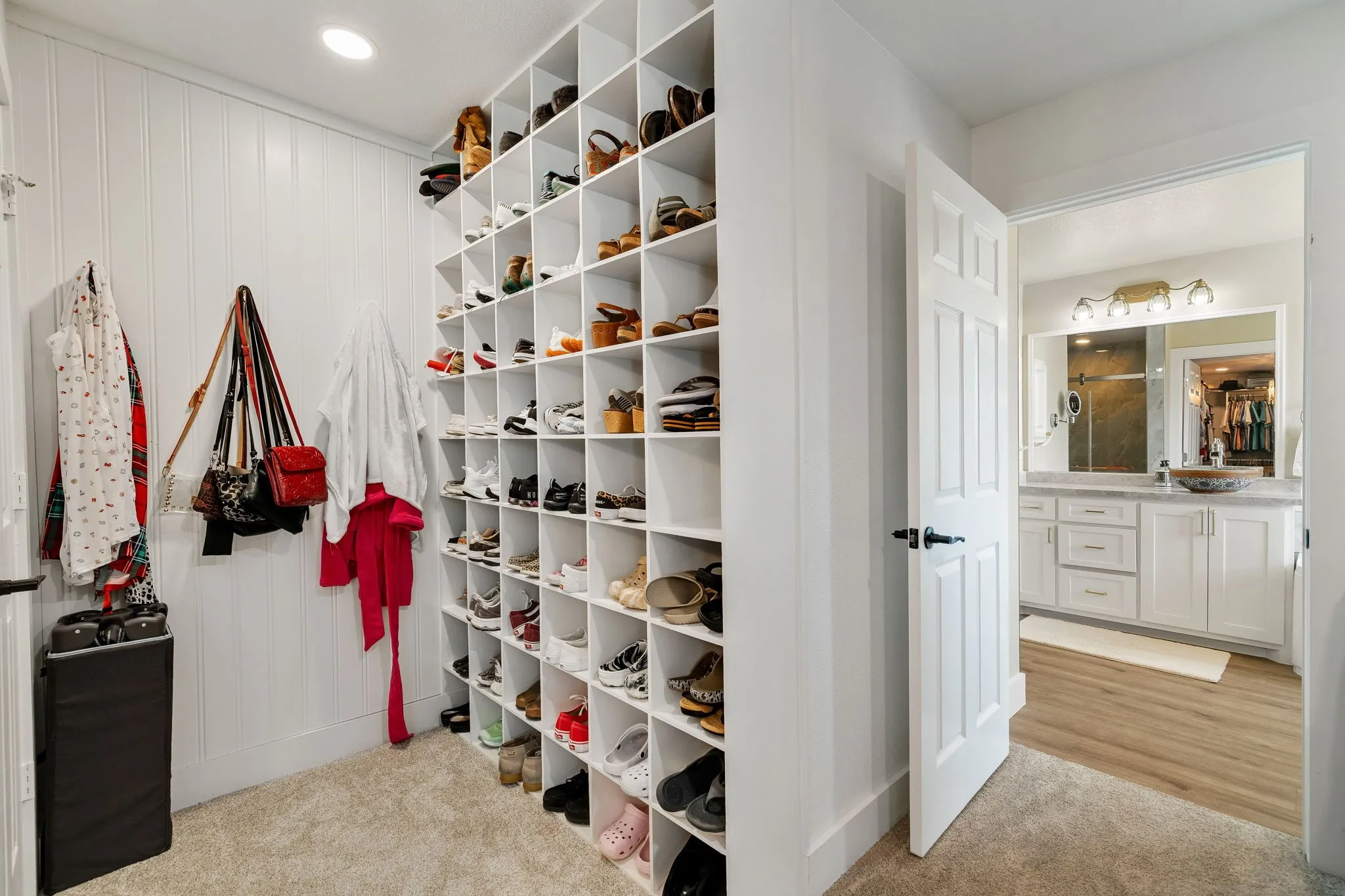 Custom built-in shoe storage with individual cubbies, soft carpet flooring, white paneled walls, and recessed lighting