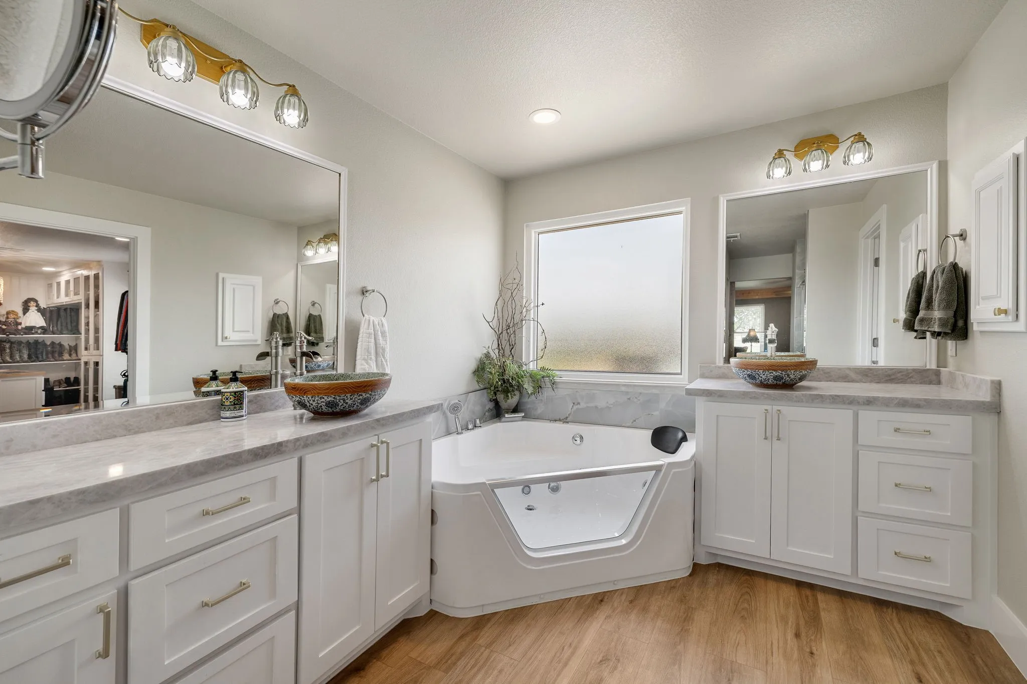 Contemporary bathroom featuring dual vanity stations with vessel sinks, white cabinetry, and light-toned countertops