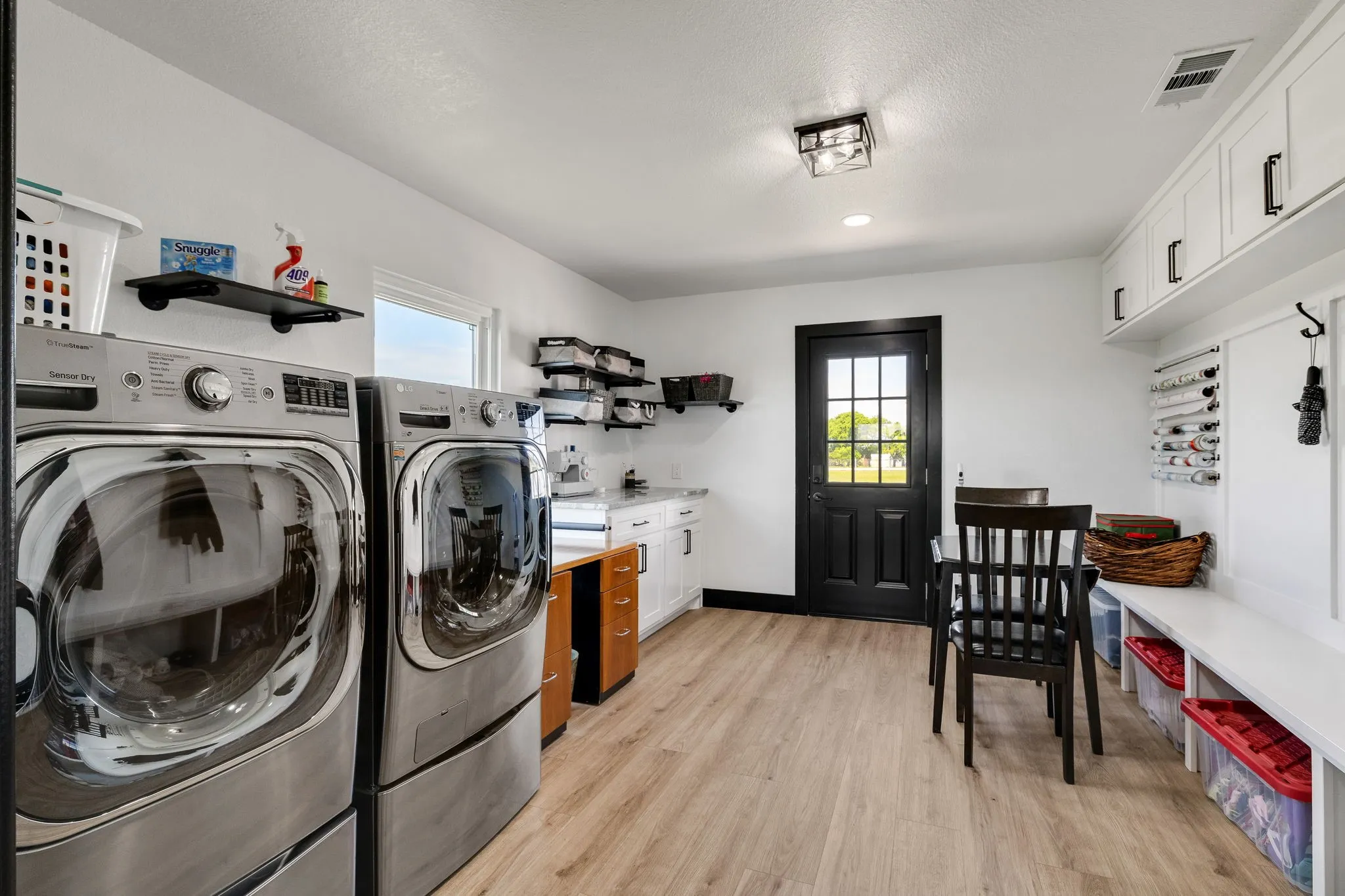 Laundry area with wood-finish flooring, white cabinetry, a built-in bench, and a black paneled door with glass inserts