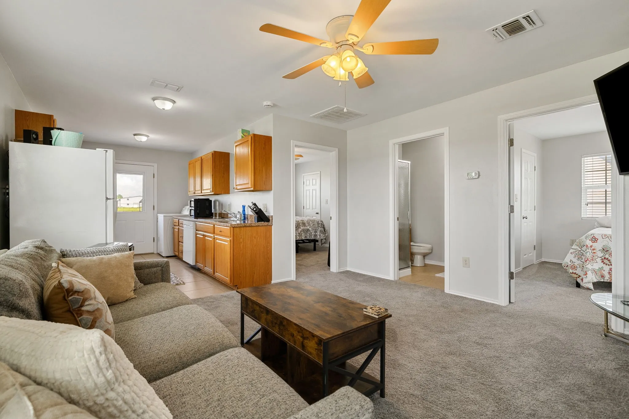 Open-concept living area featuring light gray walls, carpet flooring, and a ceiling fan with integrated lighting