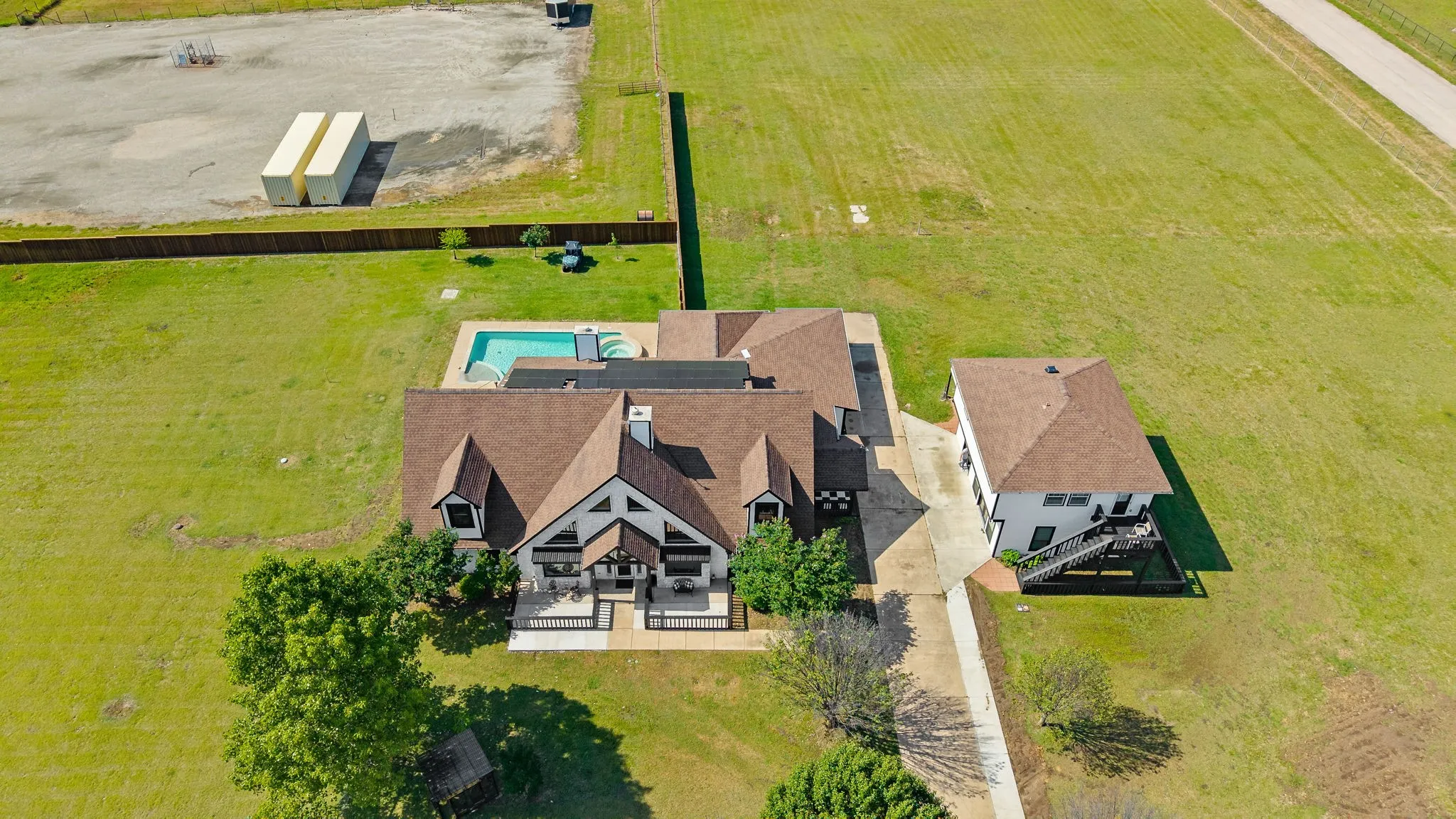 Expansive property featuring a main residence with a gabled roofline, a detached secondary structure, a swimming pool, and extensive grassy areas