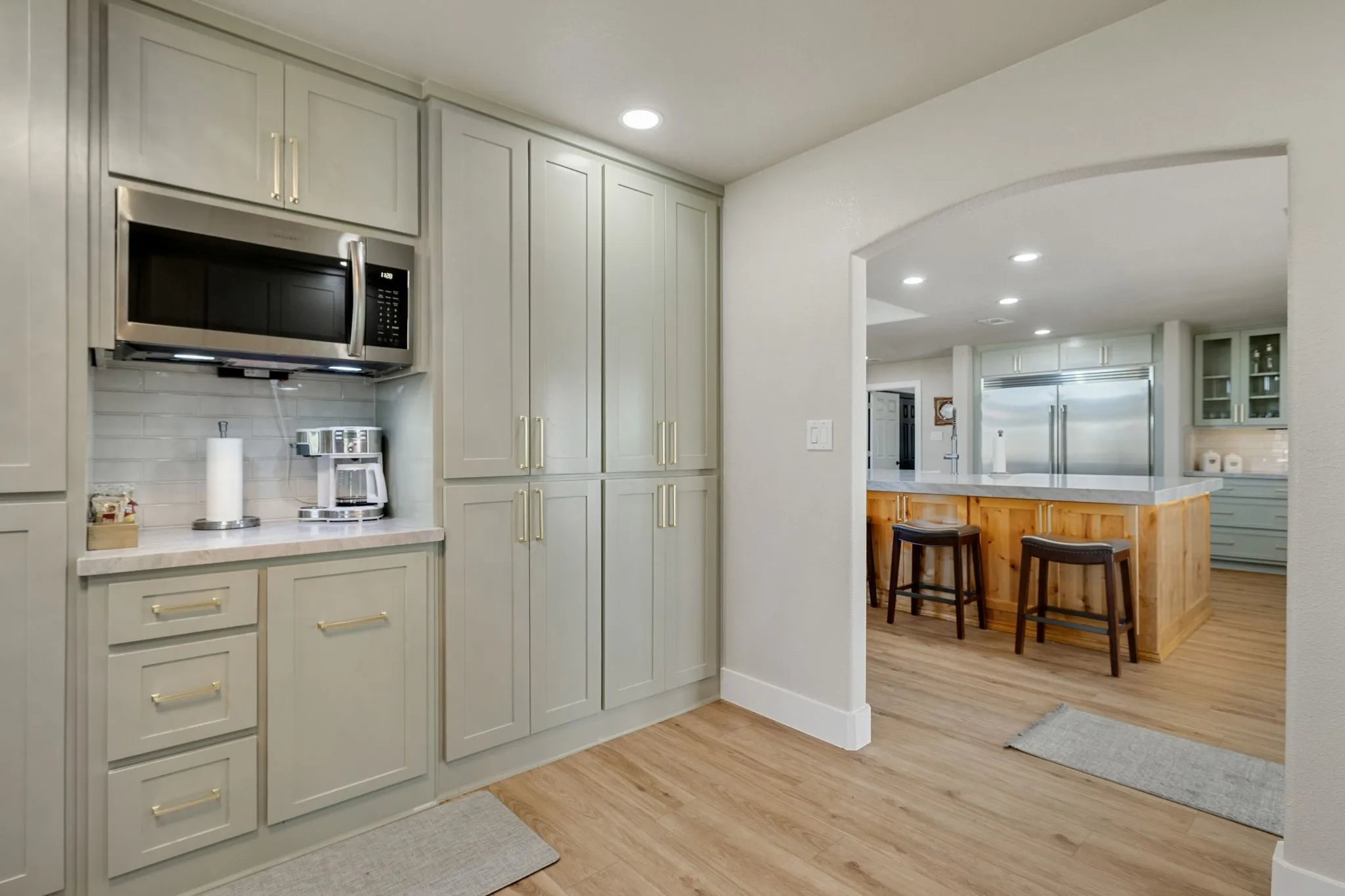 Kitchen featuring extensive light gray cabinetry with gold-tone hardware, a built-in stainless steel microwave, and white subway tile backsplash