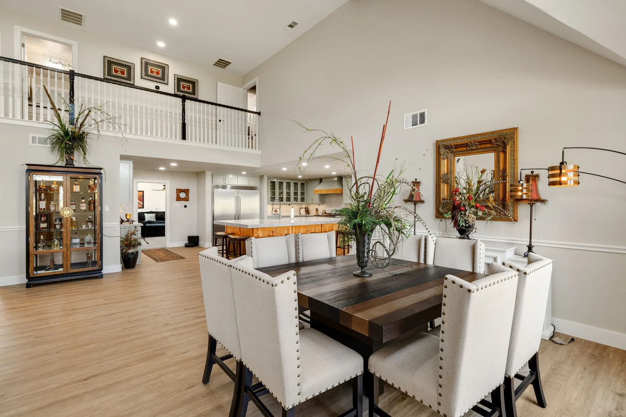 Spacious living area featuring high vaulted ceilings, light wood-finish flooring, and a second-story open balcony with white balusters