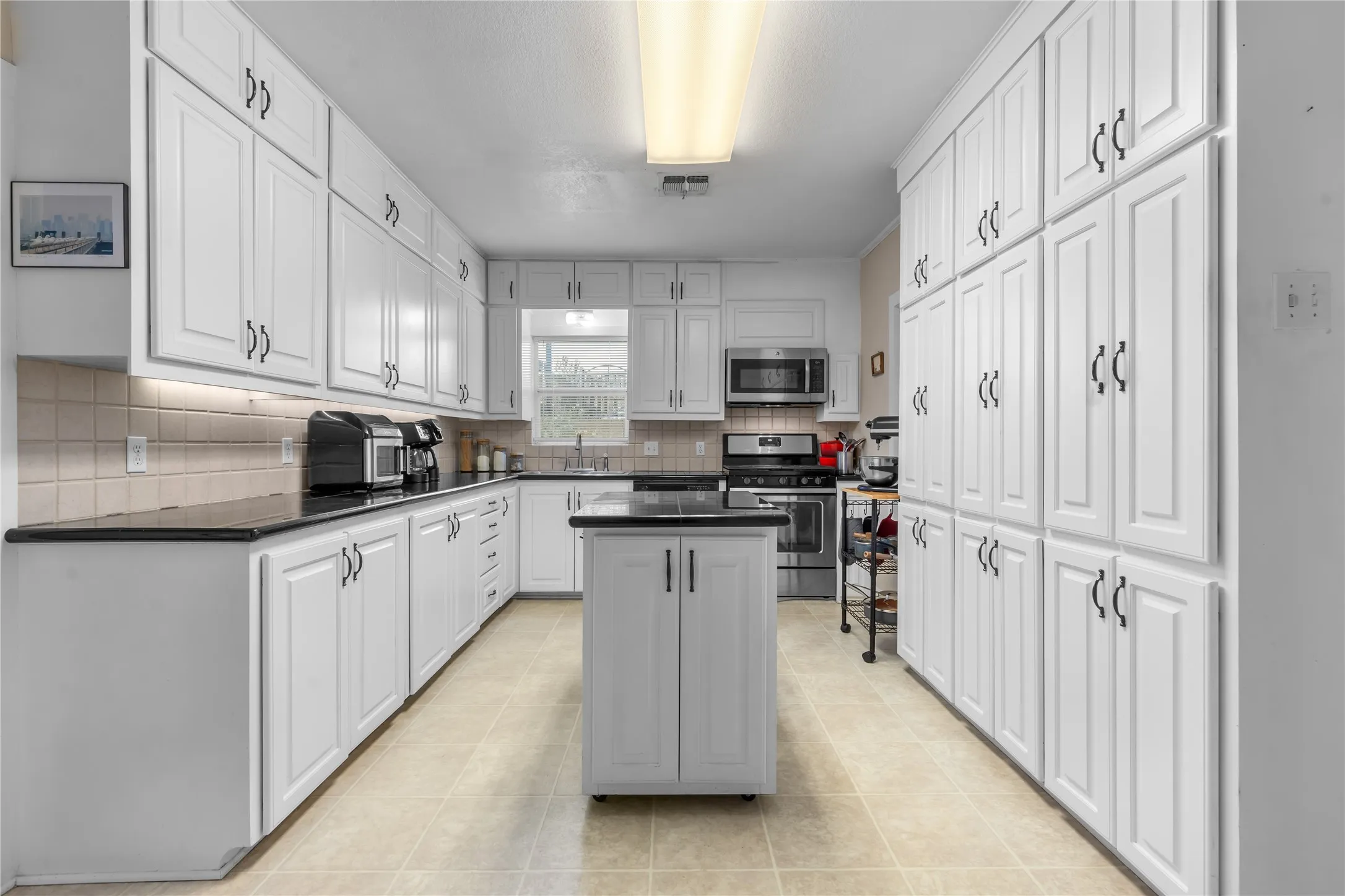 Kitchen featuring abundant white cabinetry, dark countertops, a central island, stainless steel appliances, and tile flooring