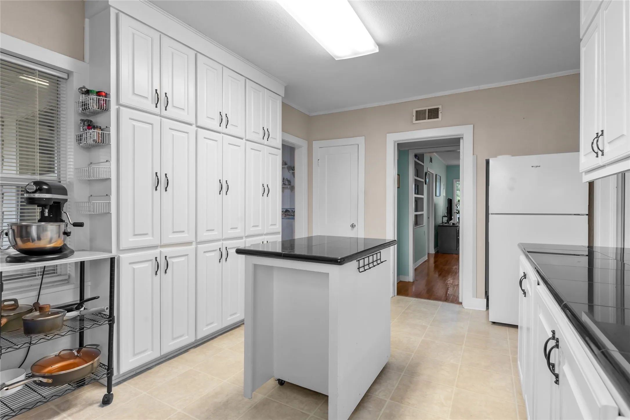 Kitchen featuring extensive white cabinetry, dark countertops, a mobile island, tile flooring, and neutral wall tones
