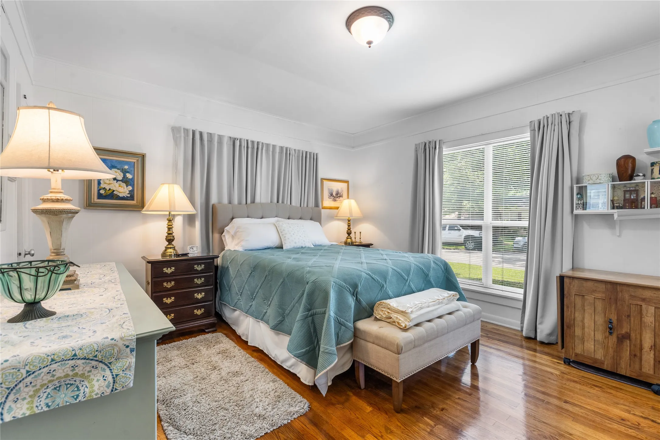 Bright room featuring hardwood flooring, a large window with privacy curtains, and crown molding
