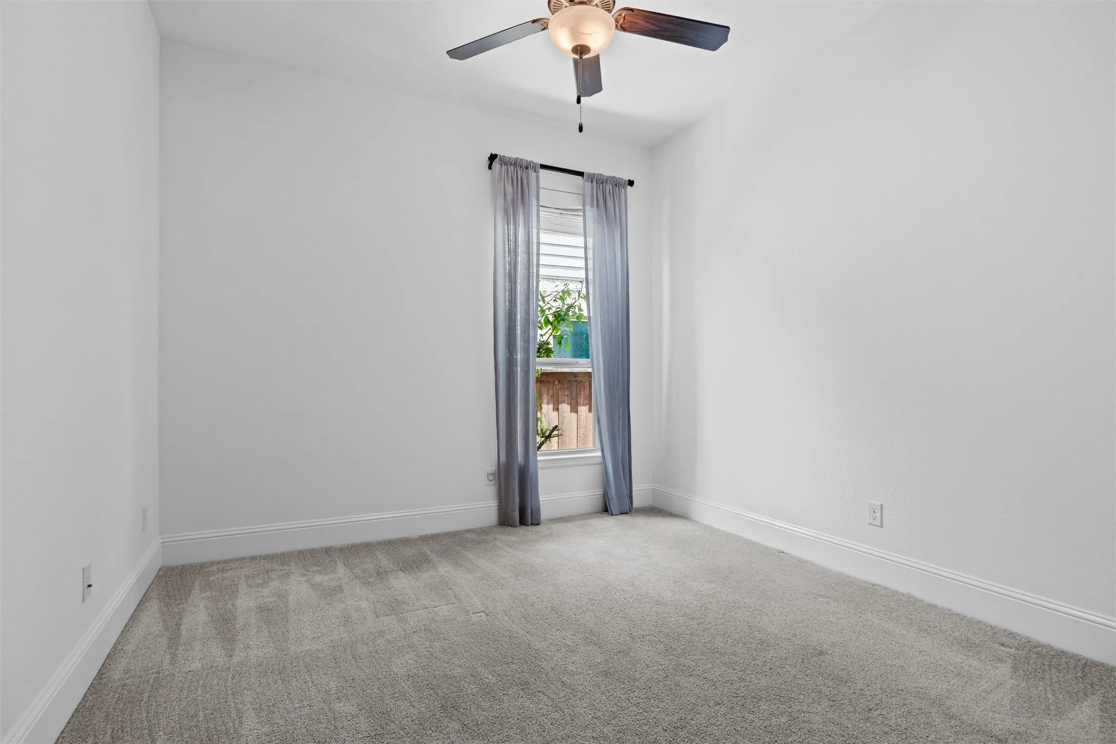This light-filled bedroom offers soft carpet, a ceiling fan, and a peaceful window view, creating a flexible space ready to grow with your needs.