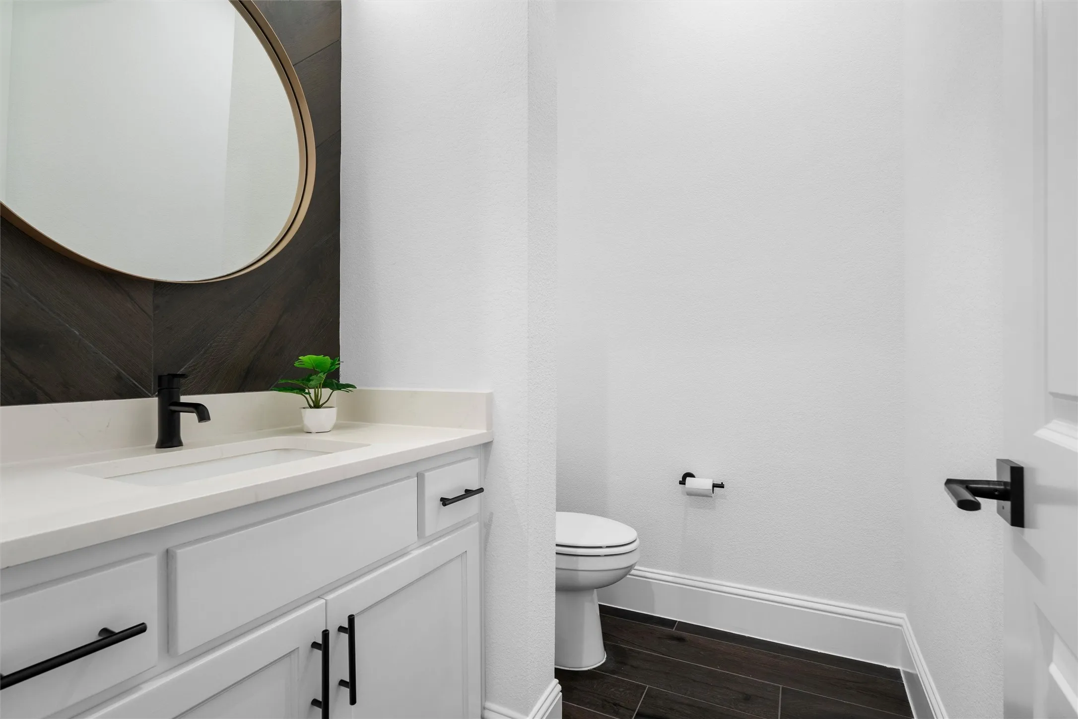 A designer powder bath adds a polished touch with a modern floating-style vanity, matte black fixtures, oversized round mirror, and rich dark accent wall that feels straight out of a luxury model home.